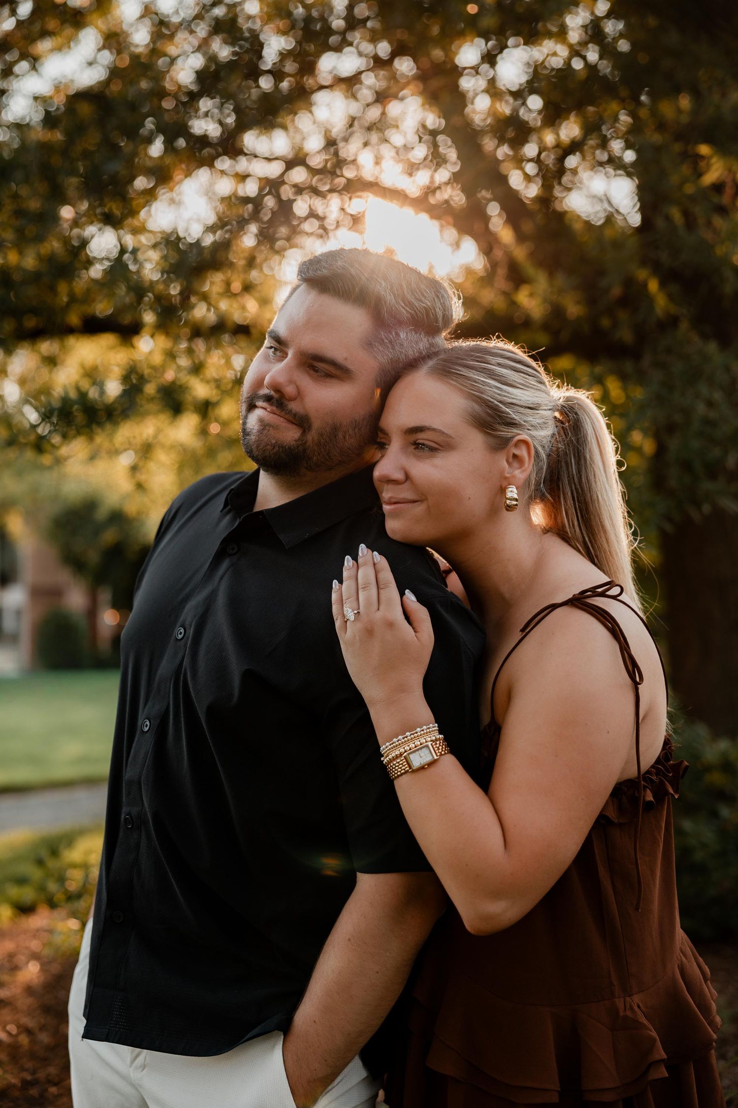 Couple embracing outdoors at golden hour, woman in brown top resting head on man in black shirt.