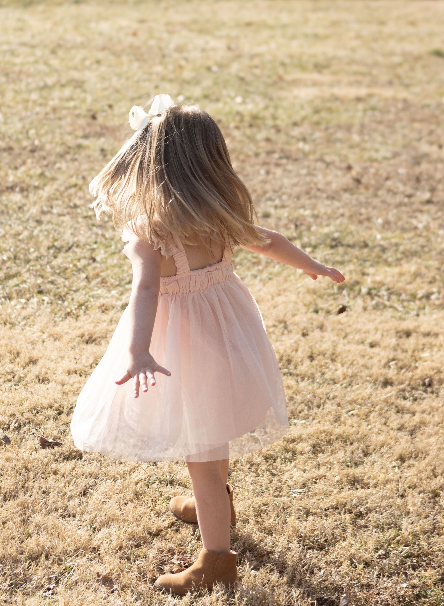 A child in a pink dress twirling joyfully in a sunlit field.