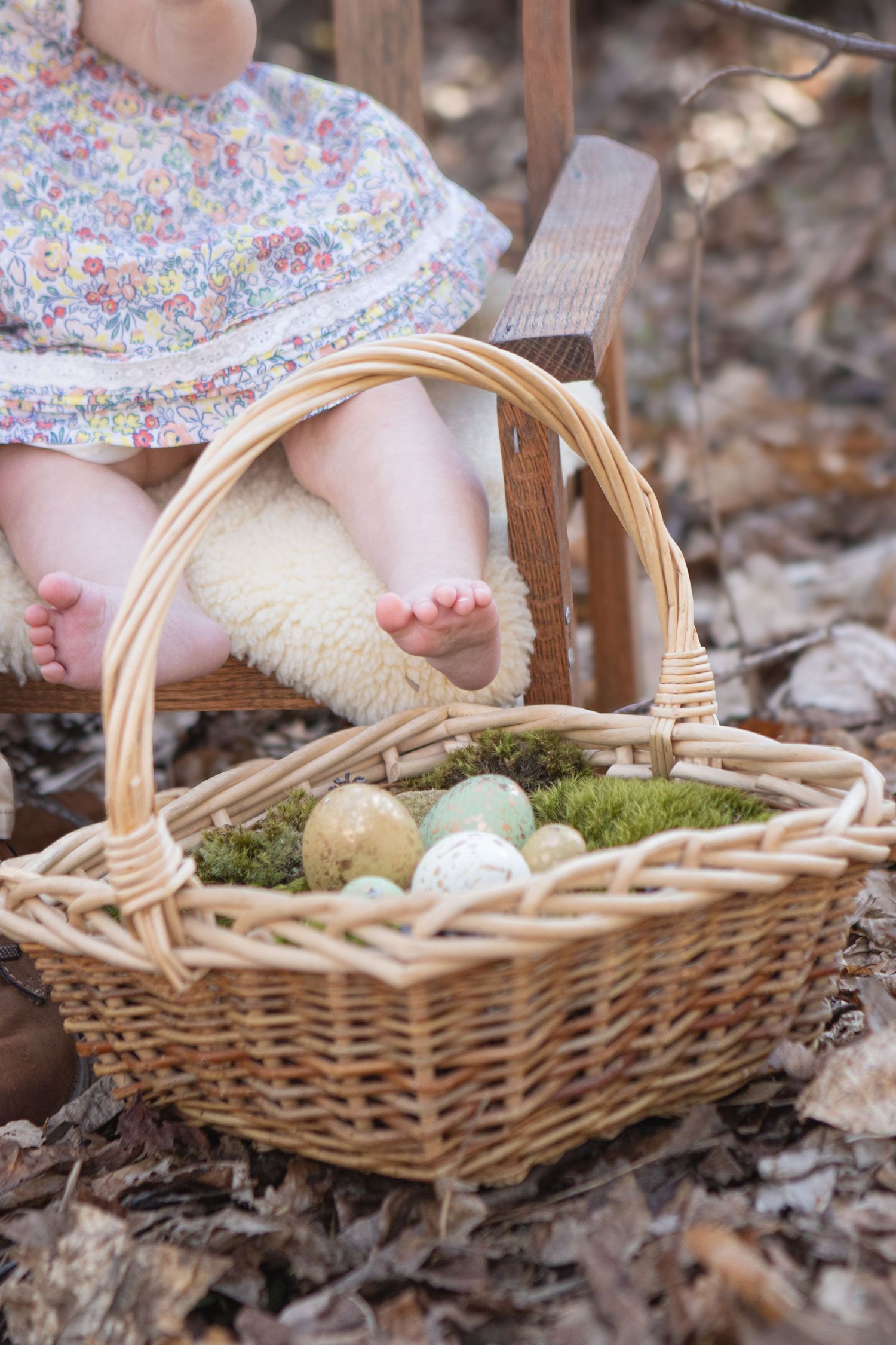Baby feet next to Easter eggs in a wicker basket with moss.