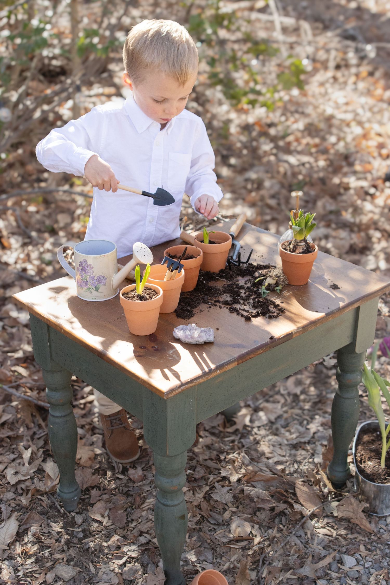 Young gardener using small tools to plant seedlings at rustic outdoor table.
