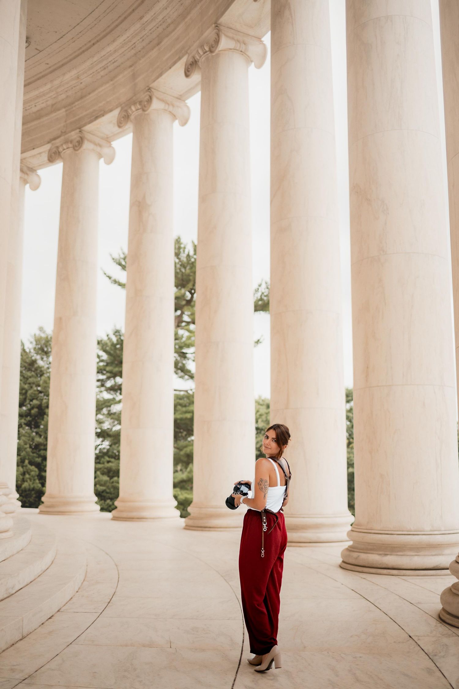 Woman in red pants and white top holding a camera among tall marble columns at the Jefferson Memorial.