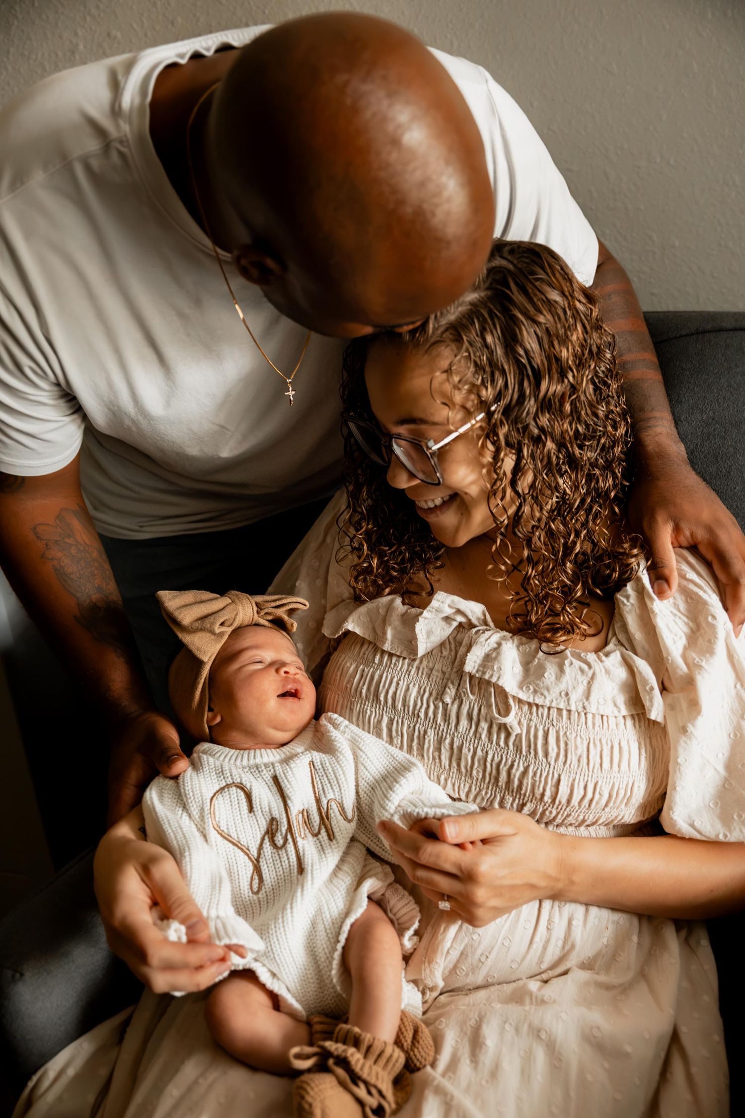 A couple lovingly gazes at their newborn baby girl in a cream outfit and bow headband.
