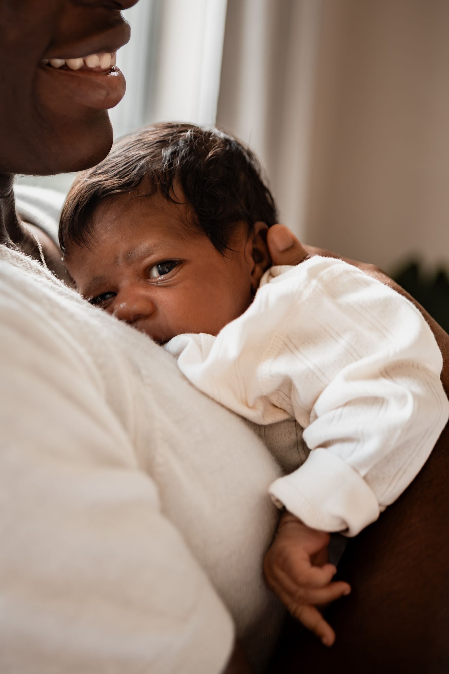Tender moment captured of an infant being held closely against a white cloth in natural lighting.