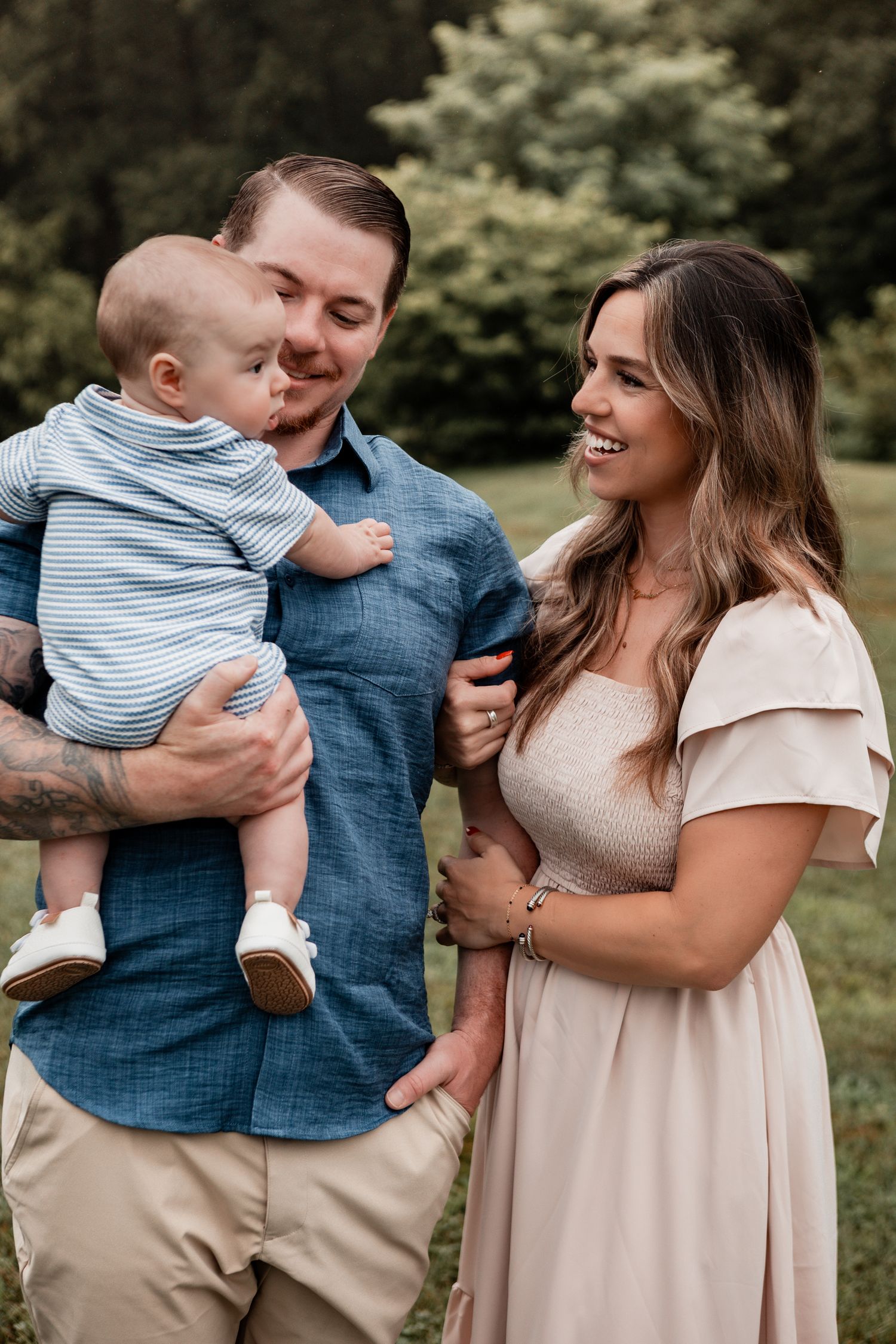 Young family wearing casual blue and beige outfits poses together outdoors in a natural setting.