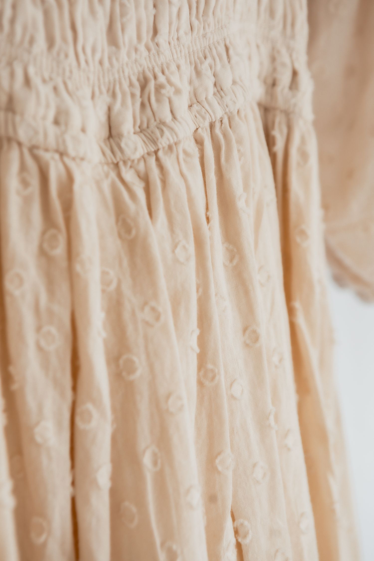 Delicate cream-colored vintage dresses hanging in a row showing intricate lace and embroidery details.