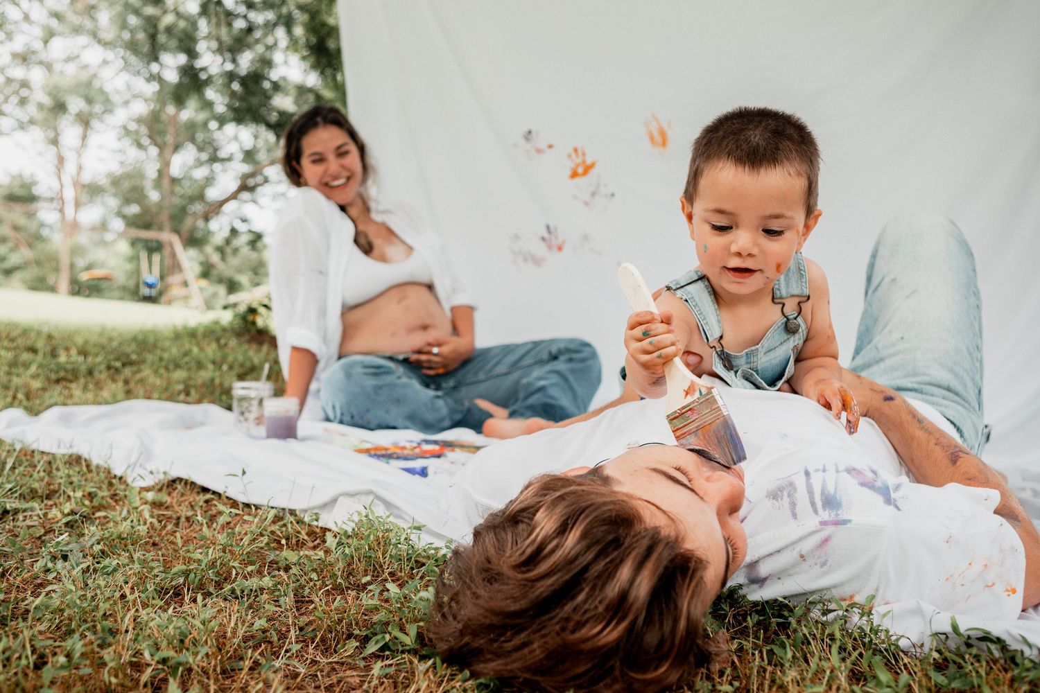 Joyful group relaxes on white blanket in grass during casual outdoor picnic on sunny day.