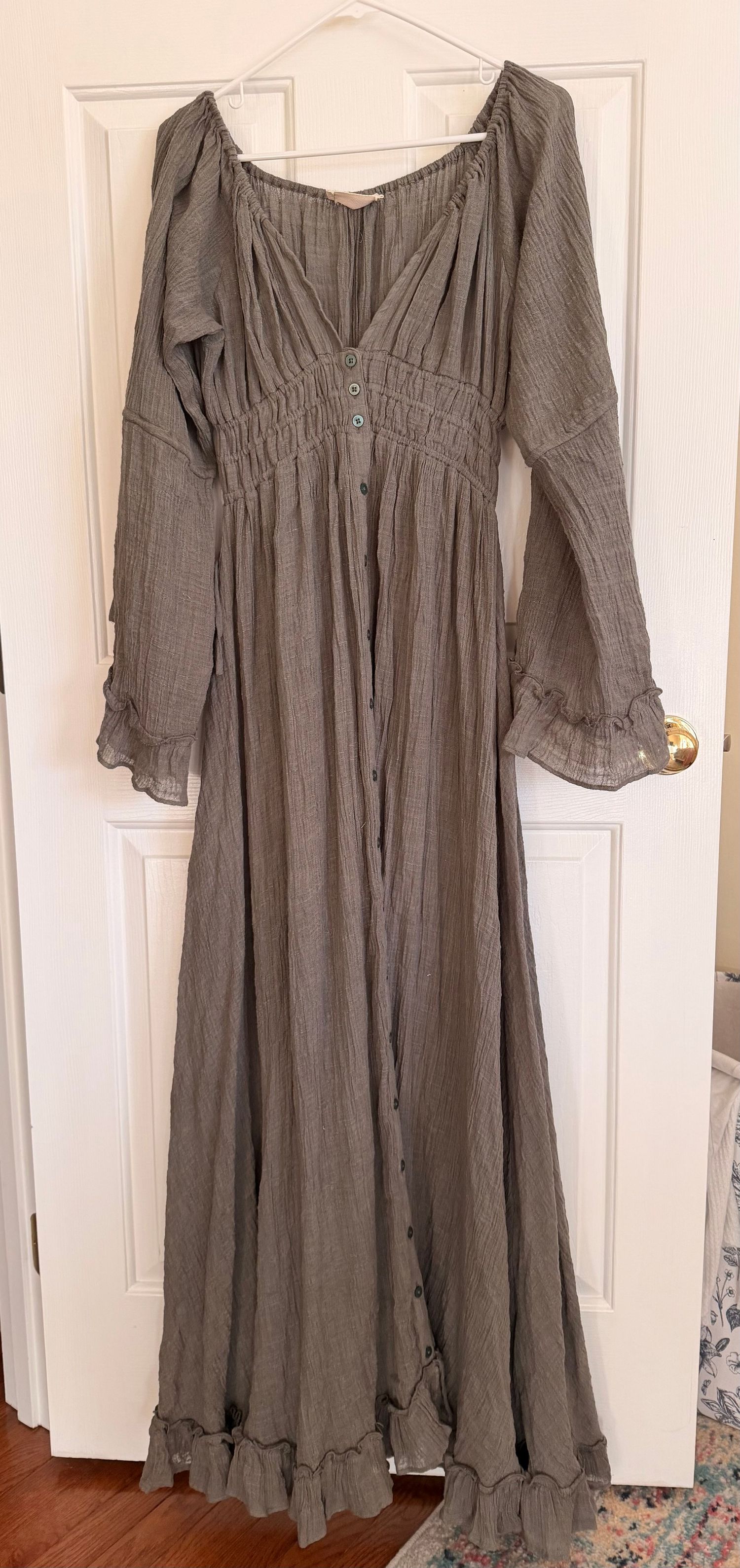 A vintage-style gray maxi dress with long sleeves, empire waist, and ruffled hem hangs against a white door.