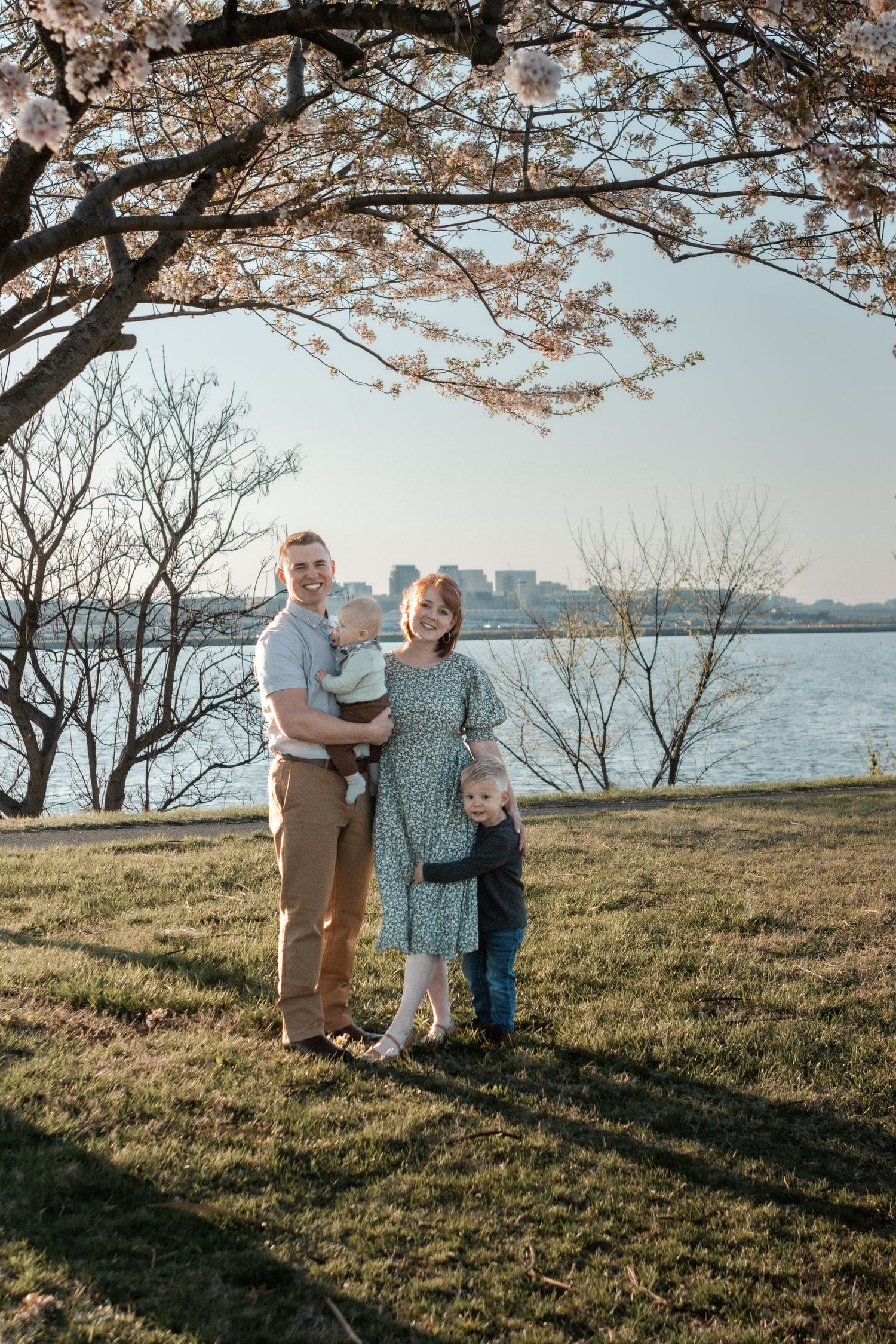 Cherry blossom trees frame a springtime family photoshoot by the waterfront at sunset.