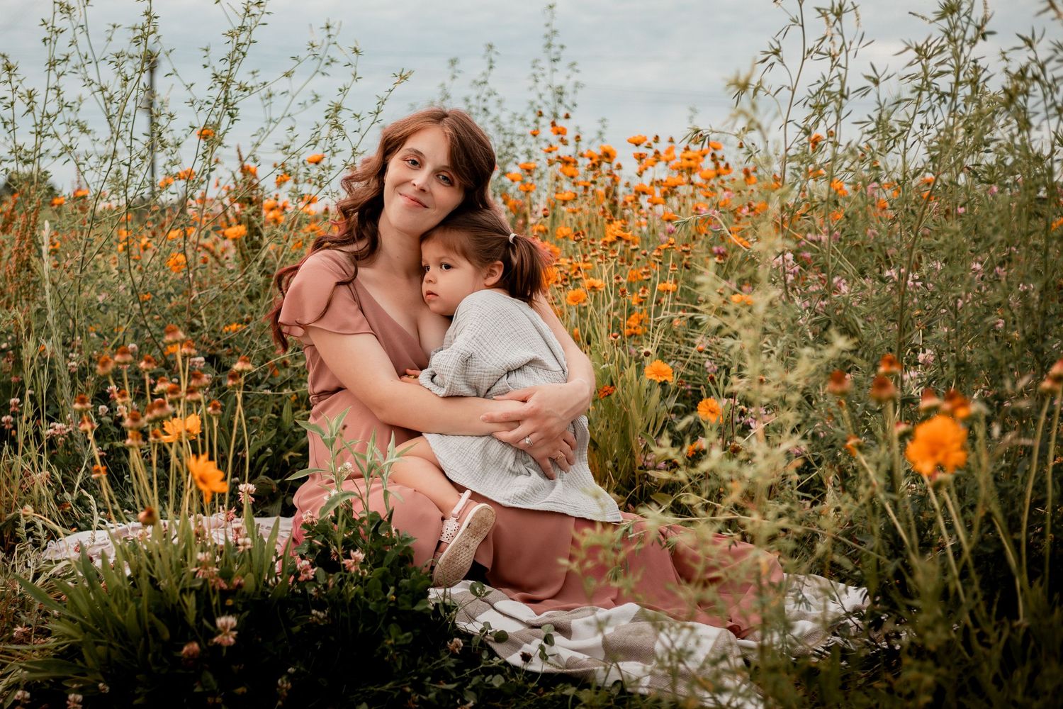 People sitting in a wildflower field with orange poppies and white wildflowers during golden hour.