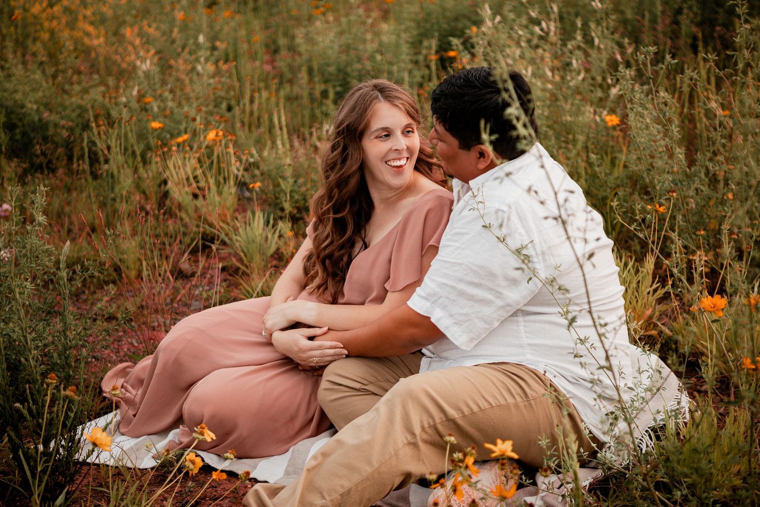 A couple relaxes together in a golden autumn meadow surrounded by wildflowers during sunset.