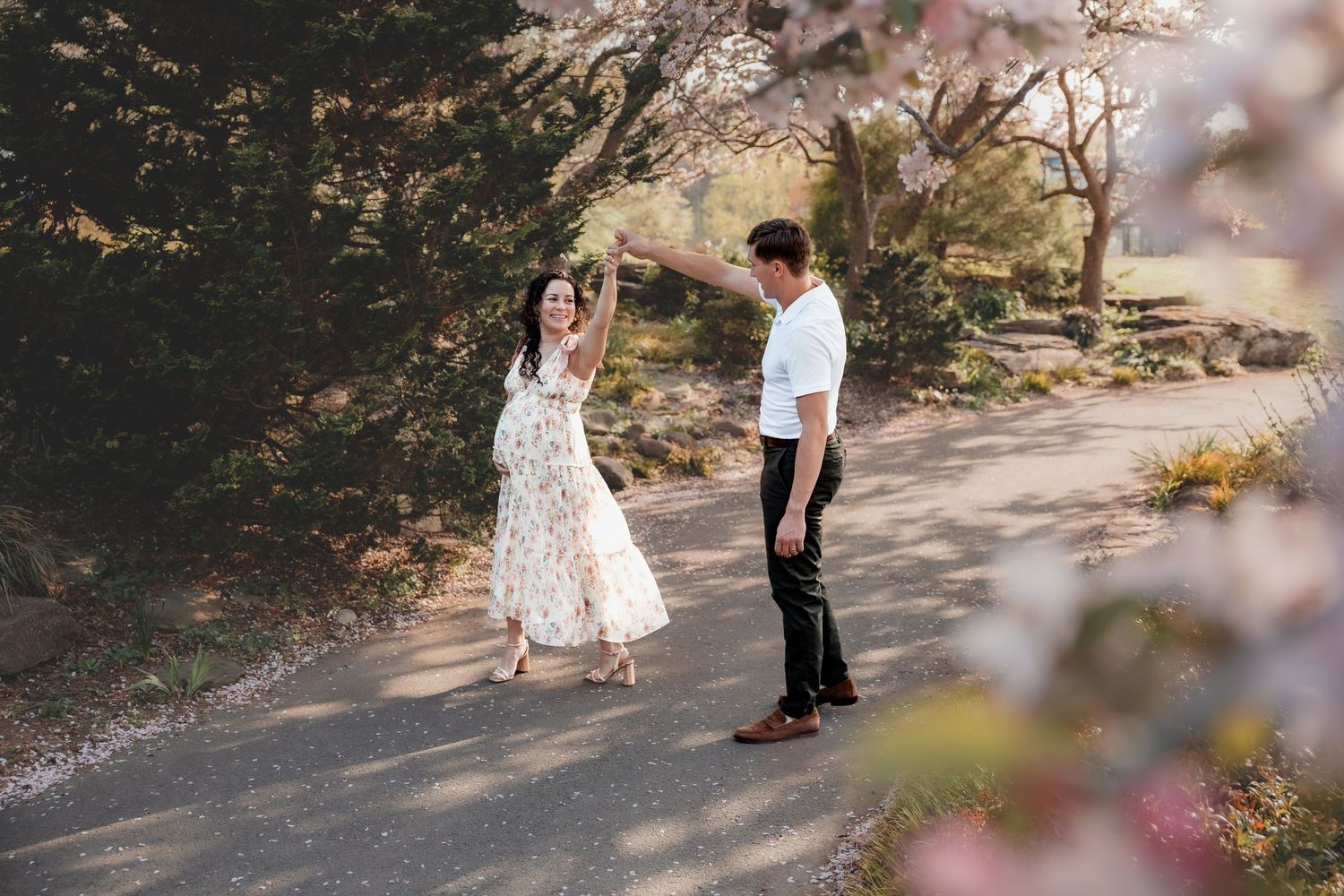 Couple dancing on a path surrounded by cherry blossom trees in full bloom during a romantic outdoor engagement session.