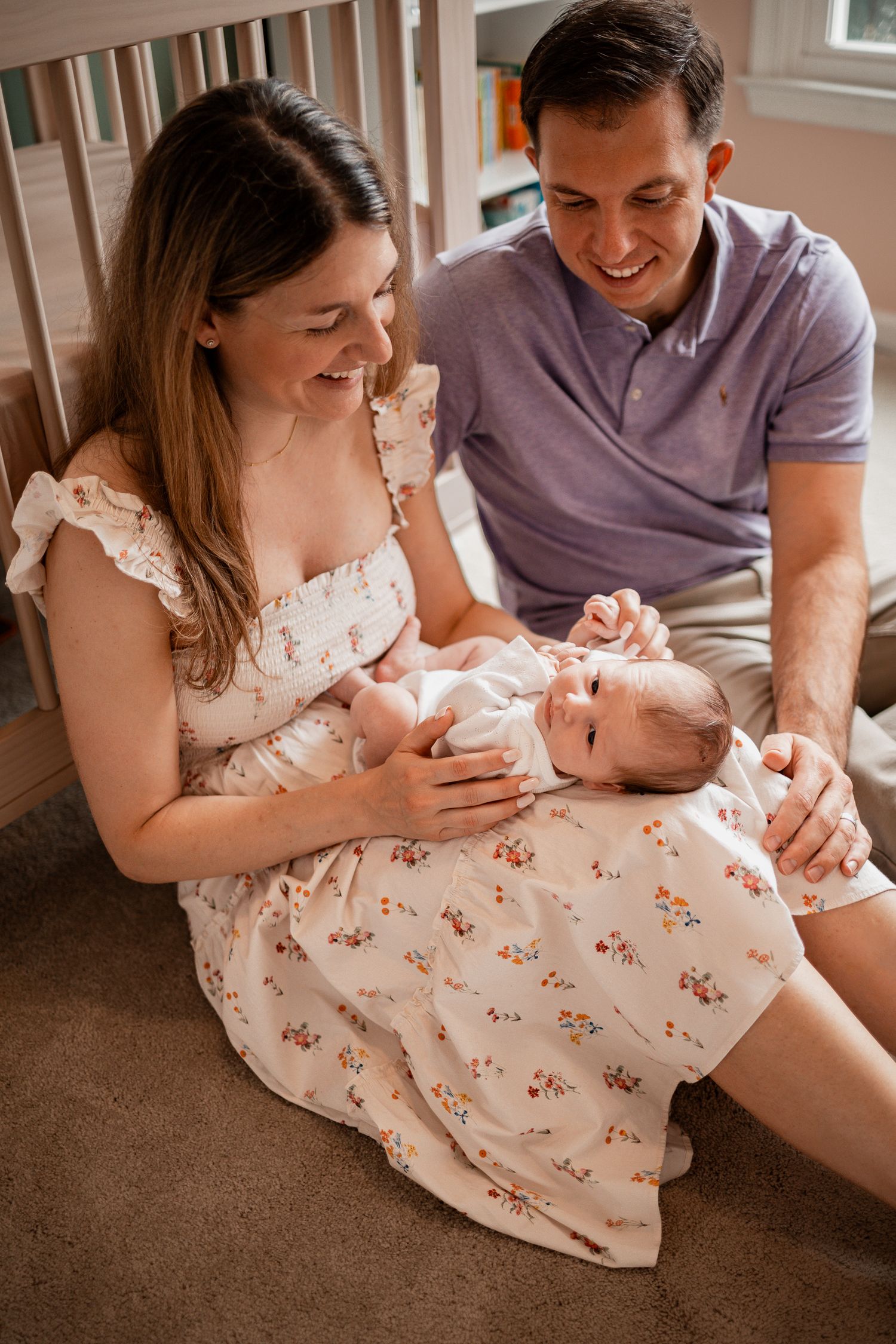 A couple sits together on carpeted floor sharing intimate moments with their newborn baby.