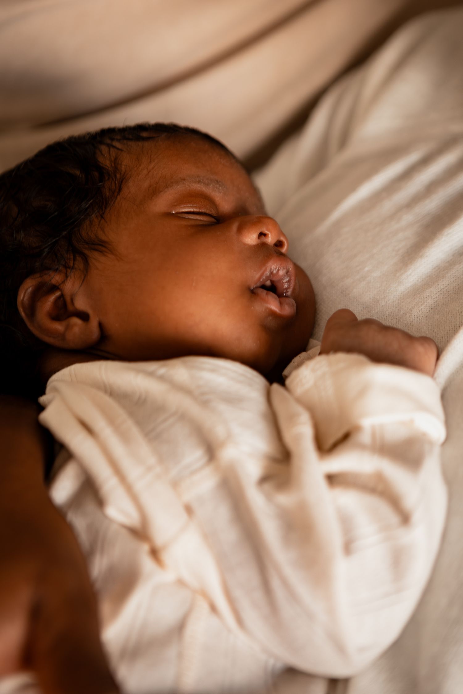 Peaceful sleeping baby in white clothing nestled in soft white bedding.