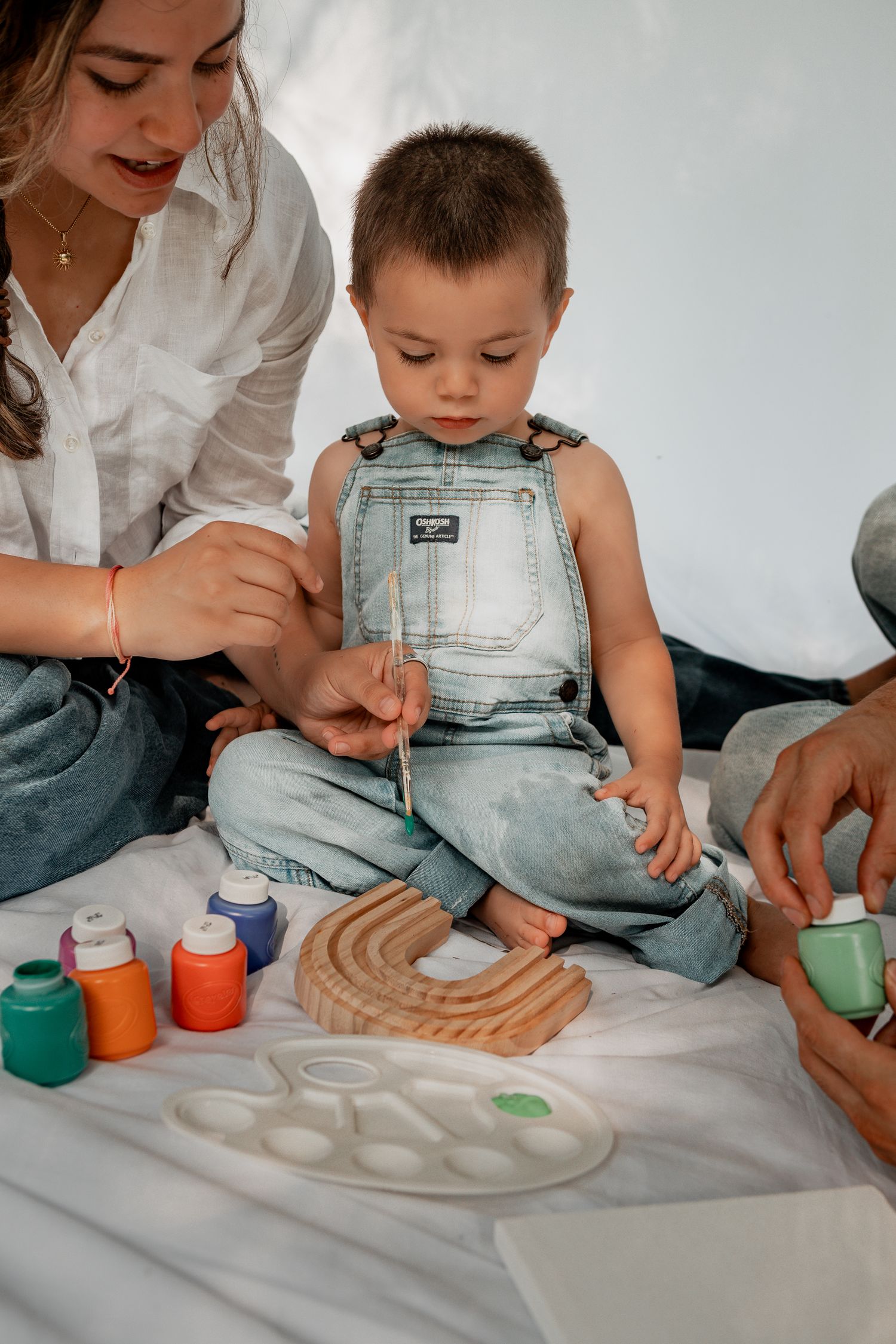 Parent and child playing together with colorful sensory activities and art materials on white surface.