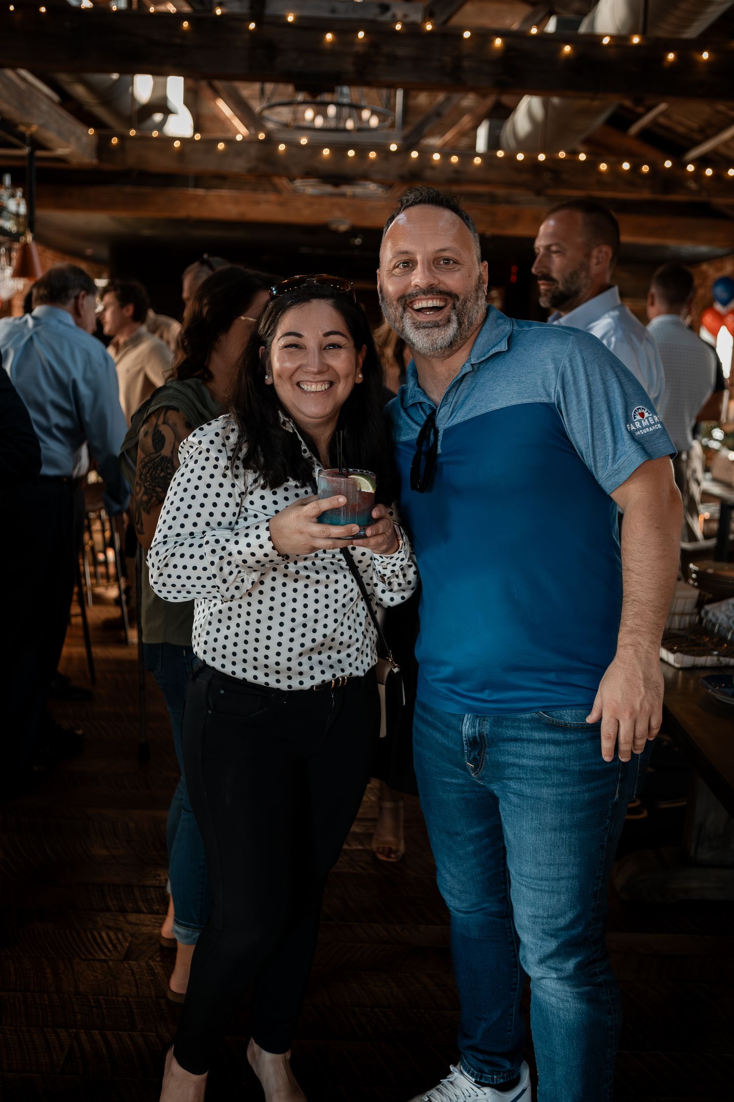 A couple embraces at a social gathering, wearing polka dots and blue casual attire.