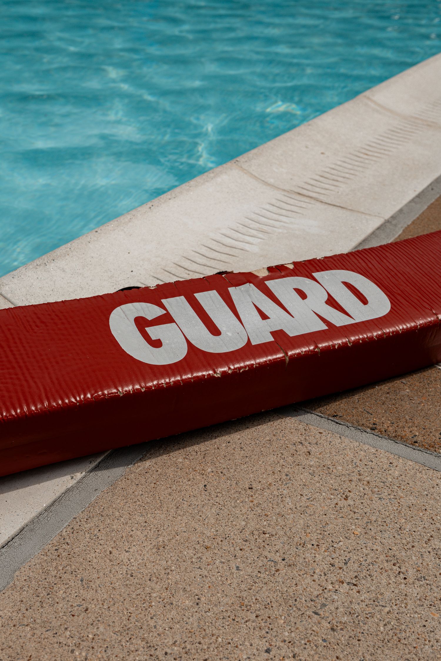 Close-up of red lifeguard flotation device next to pool edge with turquoise water.