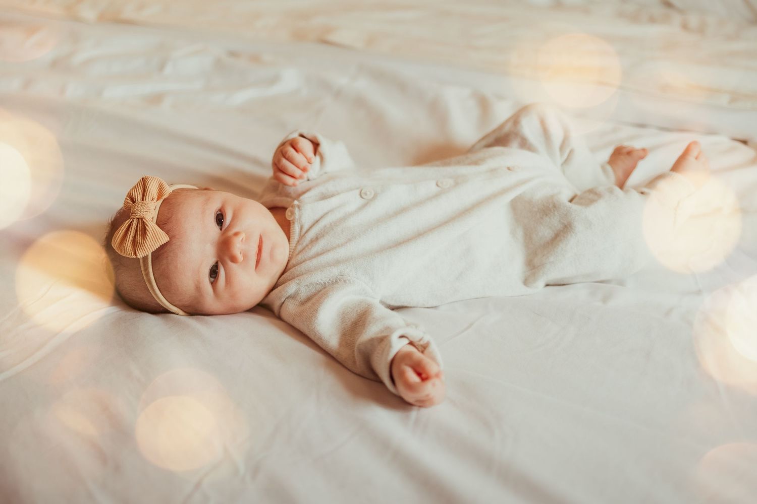 A newborn baby sleeps peacefully on soft white bedding in a dreamy, light-filled setting.
