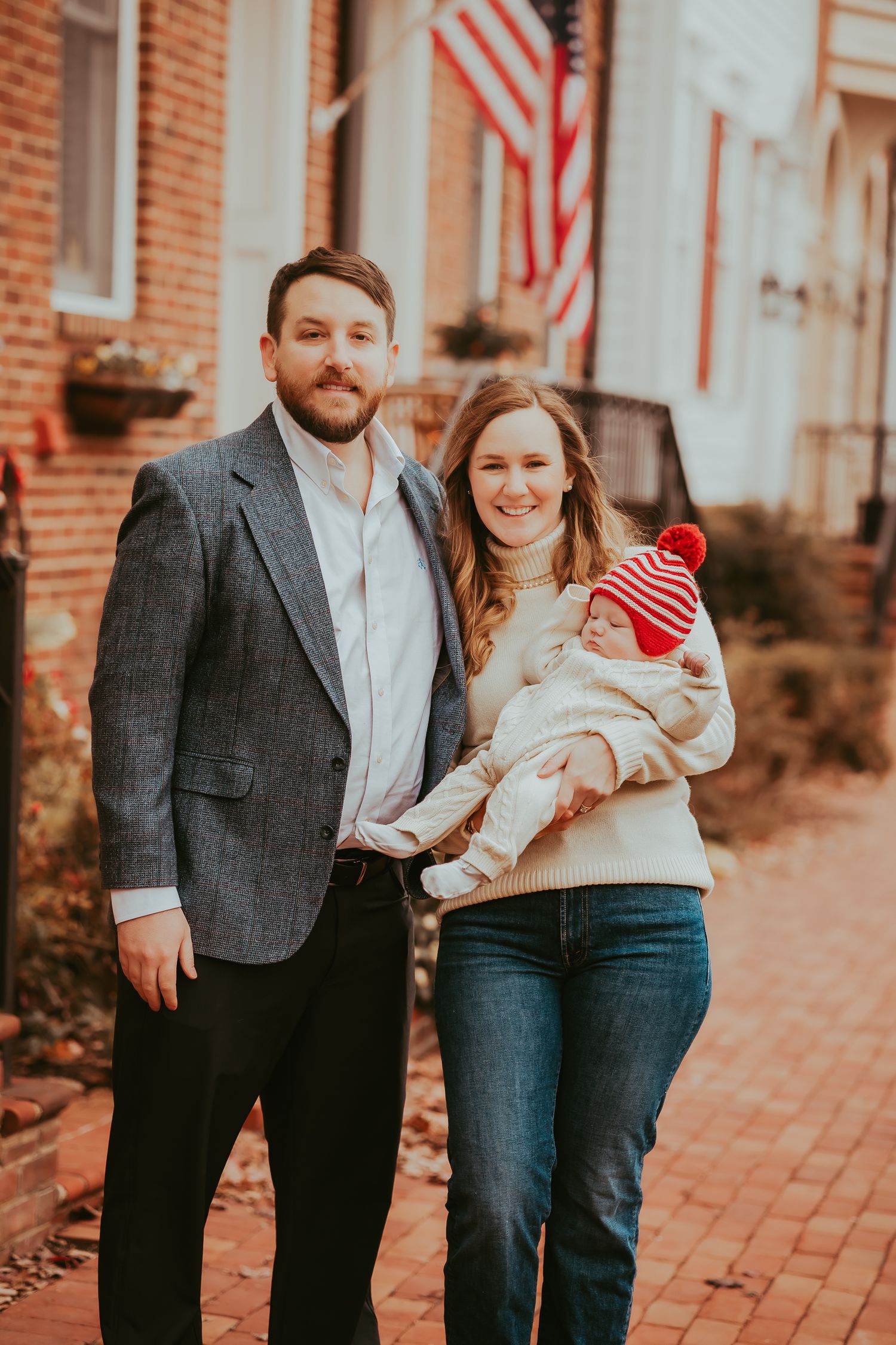 A couple poses with their baby on a brick sidewalk during an autumn photoshoot.