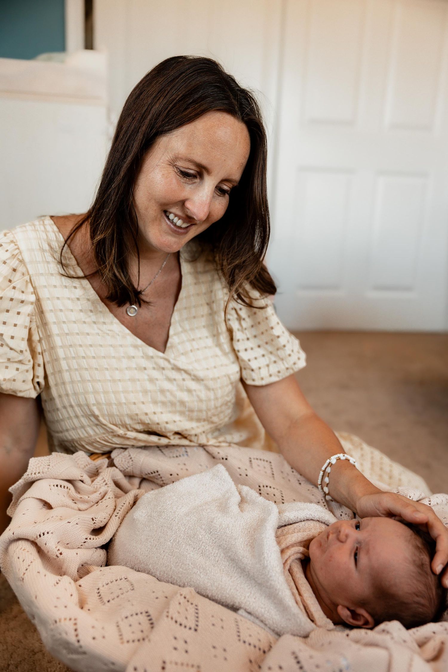 Smiling mother cradling her newborn baby wrapped in a soft pink blanket, sharing a tender moment at home.