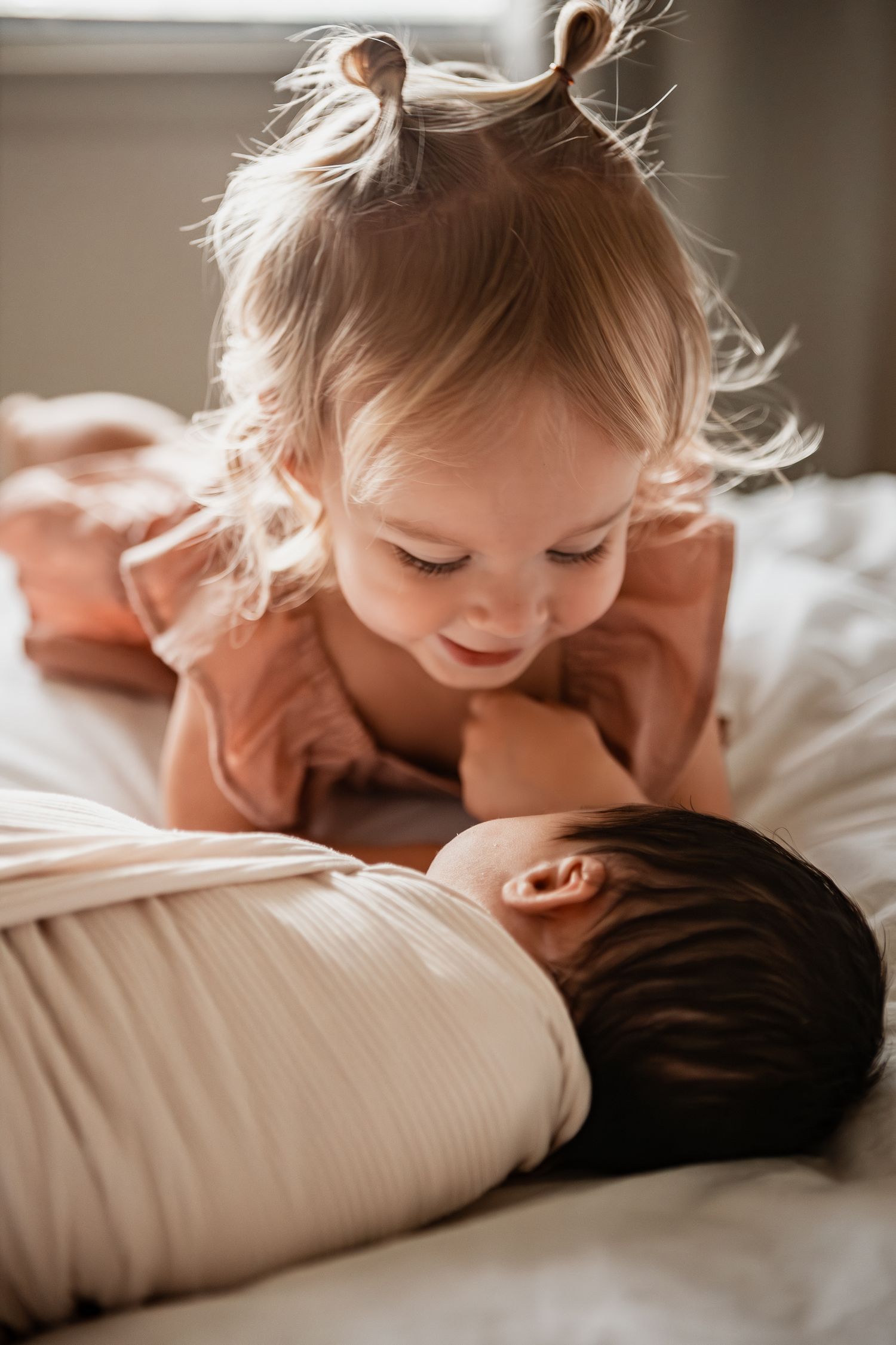 A child nestles into a comfortable white pillow with gentle sunlight streaming through nearby windows.