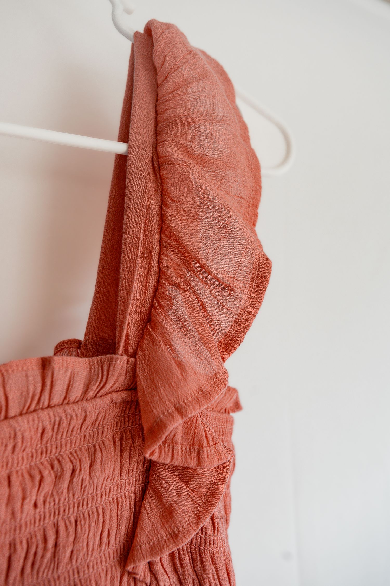 Close-up detail of pink ruffled fabric with delicate pleating and gathered texture against white background.