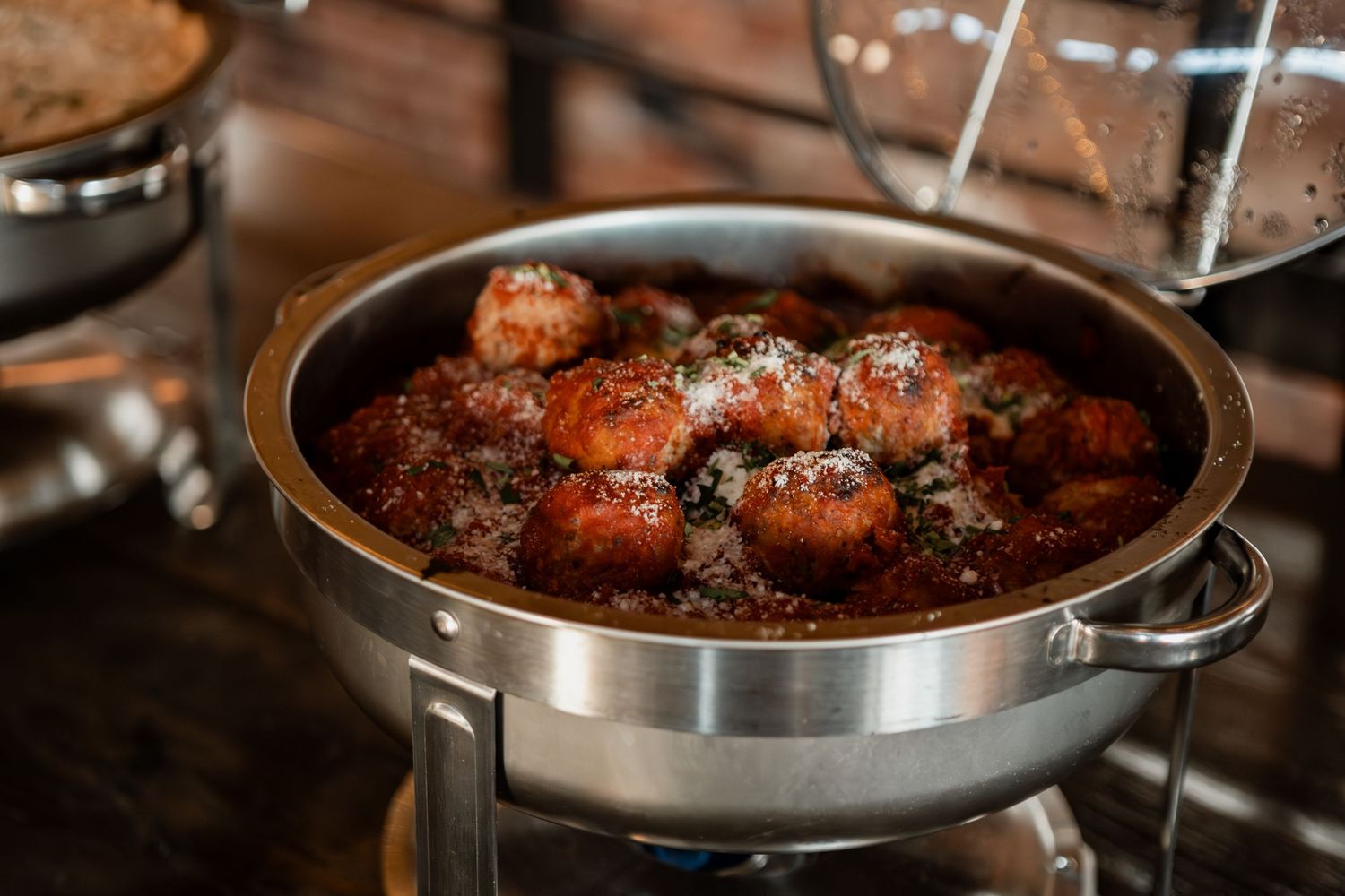 Meatballs simmering in a dark sauce in a stainless steel pan on a stovetop.