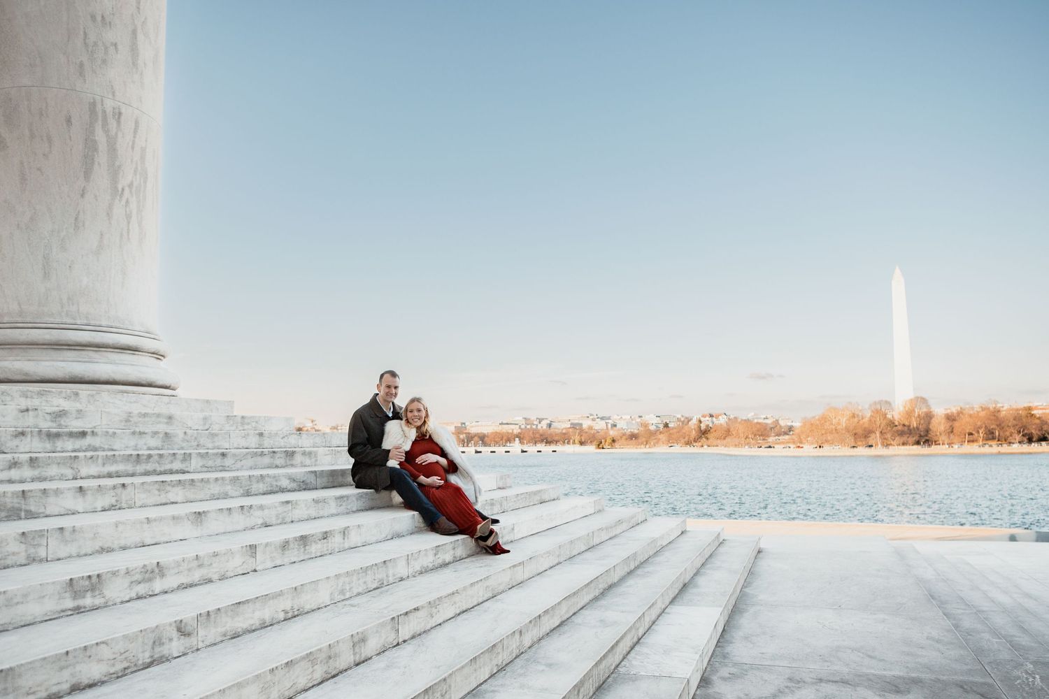 A person in red winter clothing sits alone on wide concrete steps against a bright winter sky.