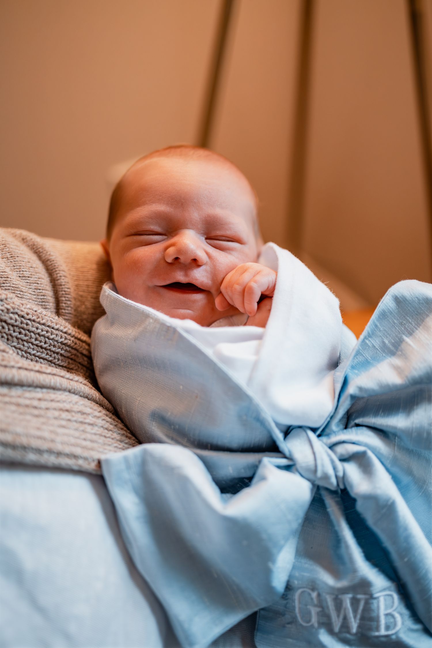 Sleeping newborn baby wrapped in light blue blanket with large bow.