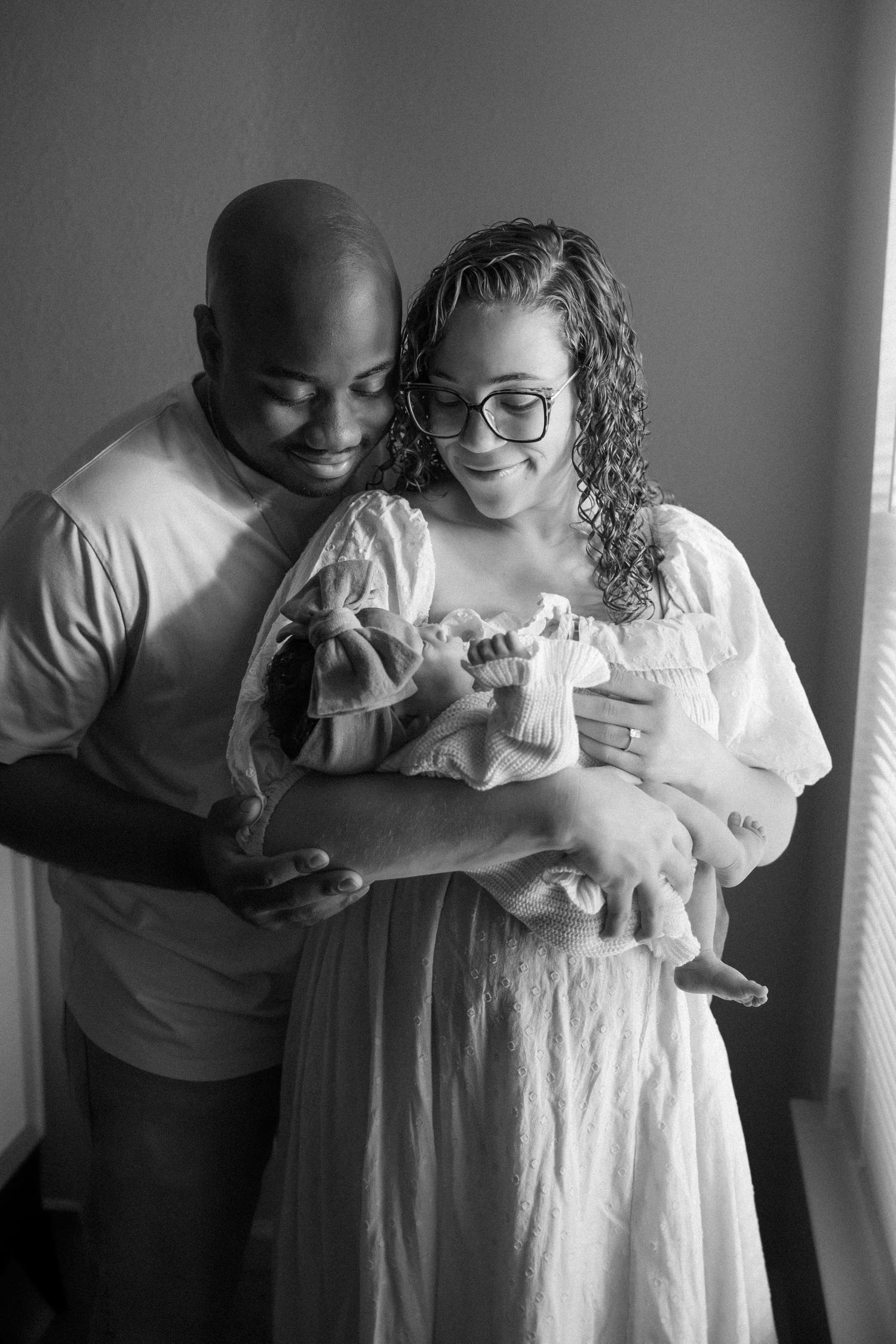 Black and white photo of a couple smiling at their newborn baby.