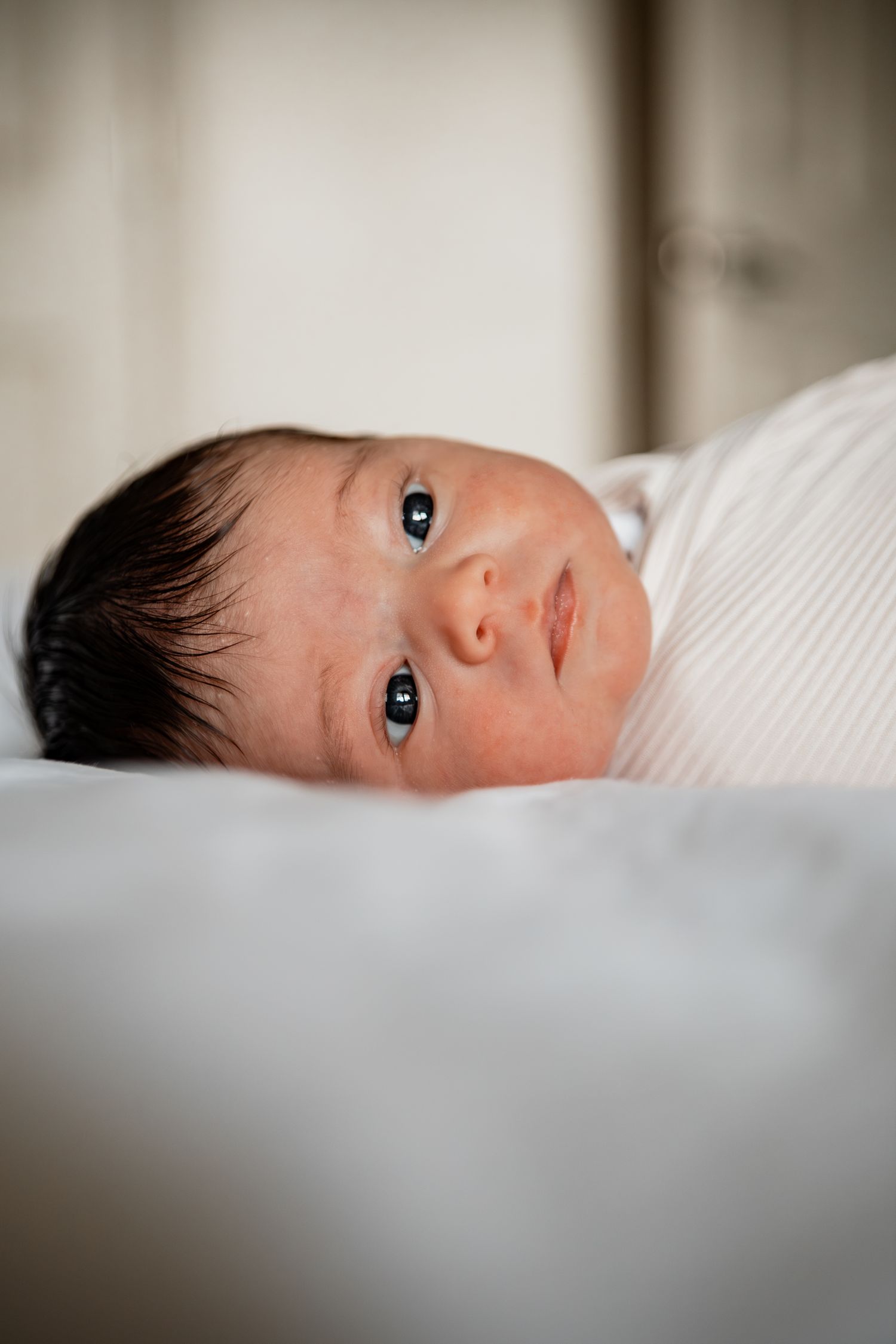 A close-up side view shows a baby lying on white bedding with soft lighting and shallow depth of field.