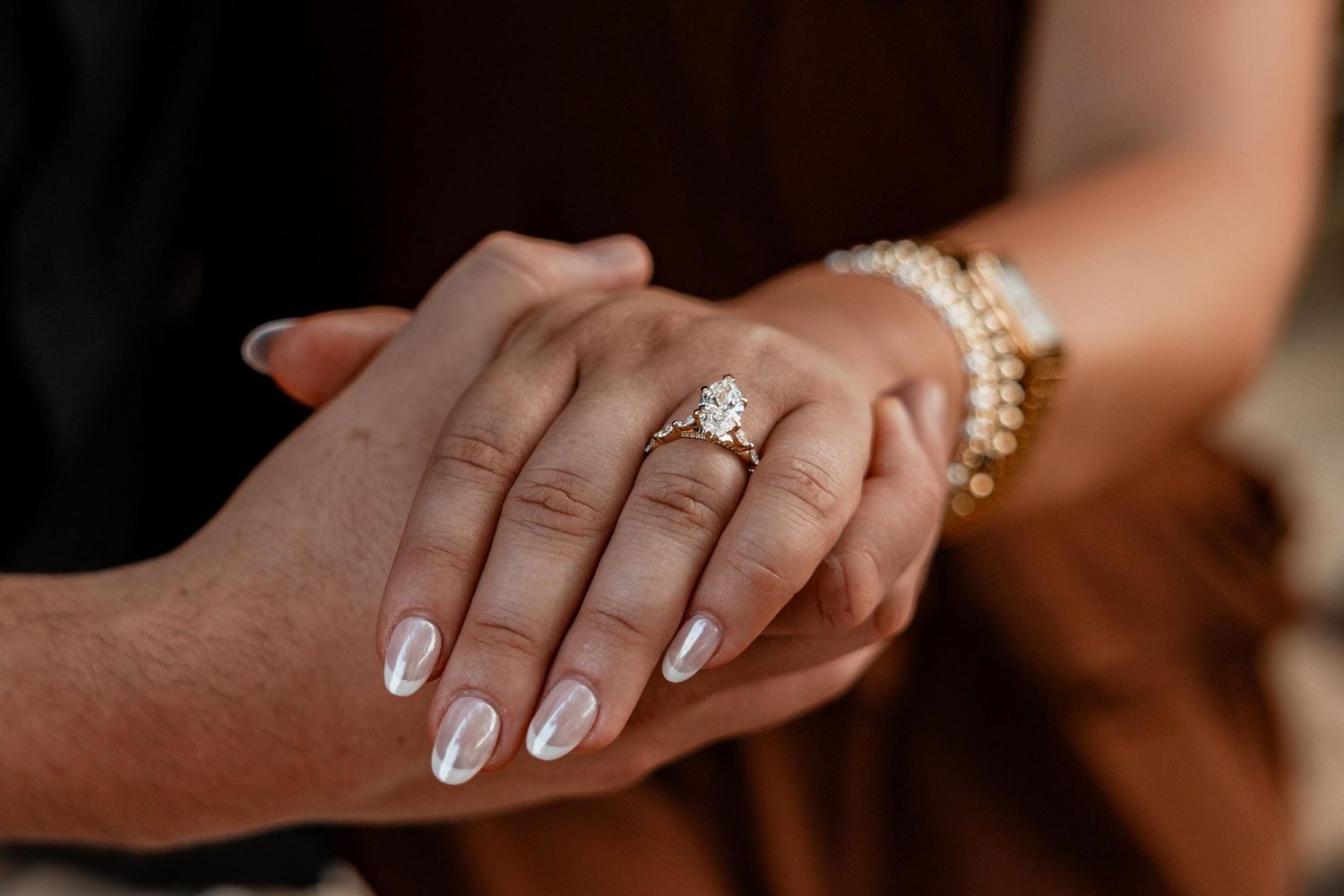 Close-up of hands showing a diamond engagement ring on a woman's finger, with a pearl bracelet on her wrist.