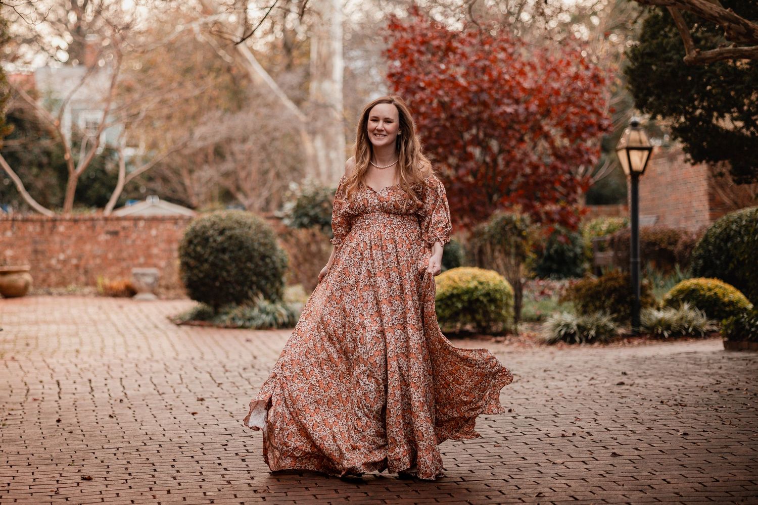 A flowing mauve dress twirls gracefully among autumn foliage and brick pathways in a romantic outdoor setting.