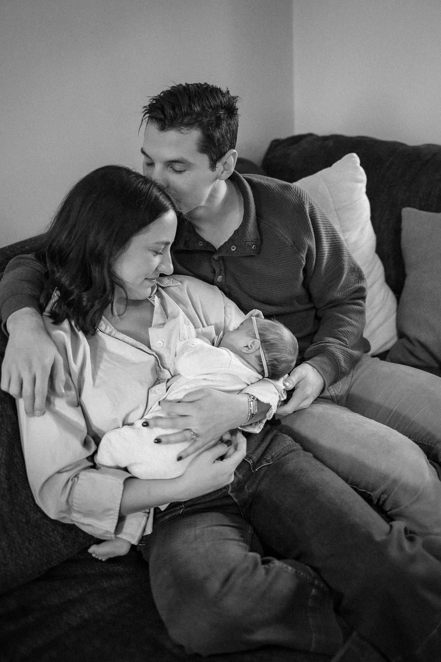 A series of black and white photographs showing tender moments between parents and their newborn baby on a couch.