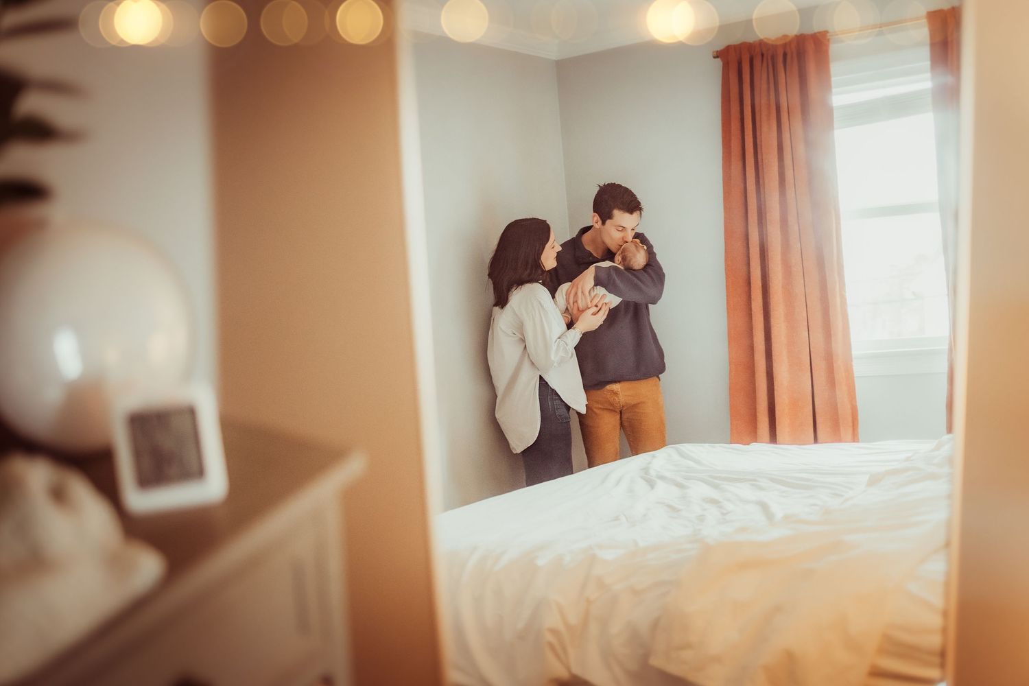 A cozy bedroom interior with warm lighting, peach curtains, and a mirror reflection showing a tender moment.