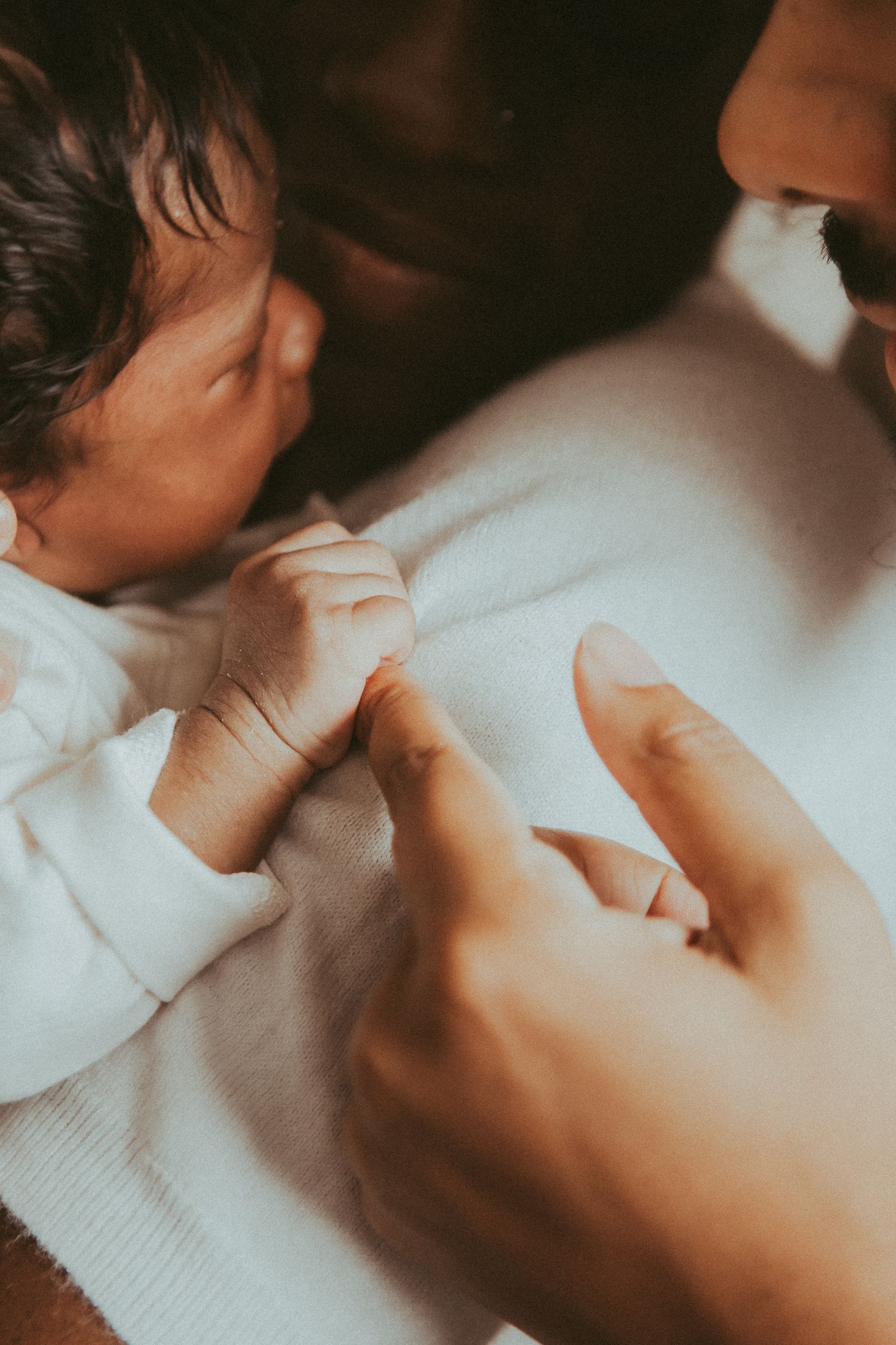 Close-up view of a tiny newborn baby's hand grasping an adult finger in warm lighting.