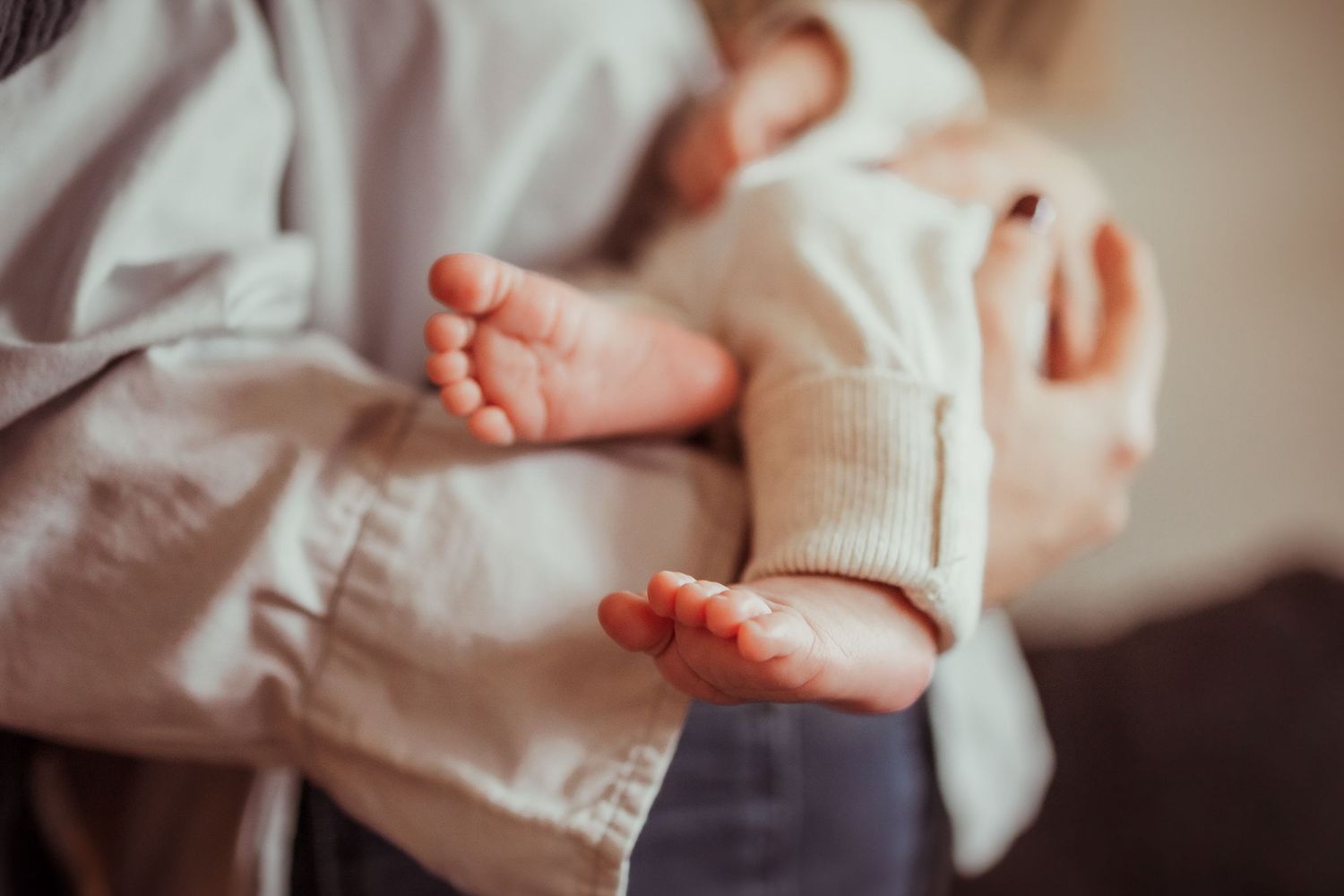 Close up of tiny newborn baby feet wrapped in soft white blanket showing delicate toes and skin texture.