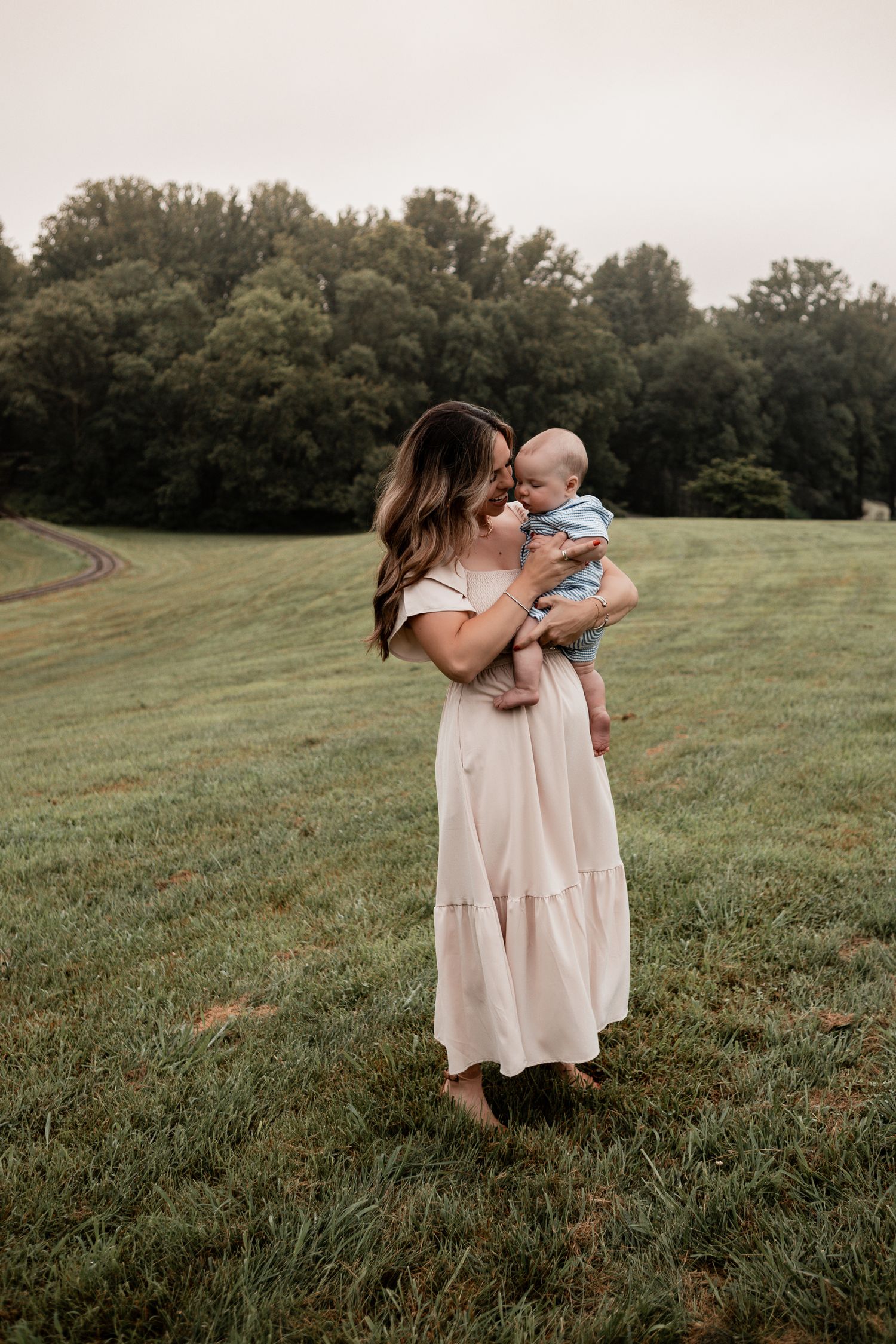 A tender moment captured on a grassy hillside during golden hour as figures embrace in soft lighting.