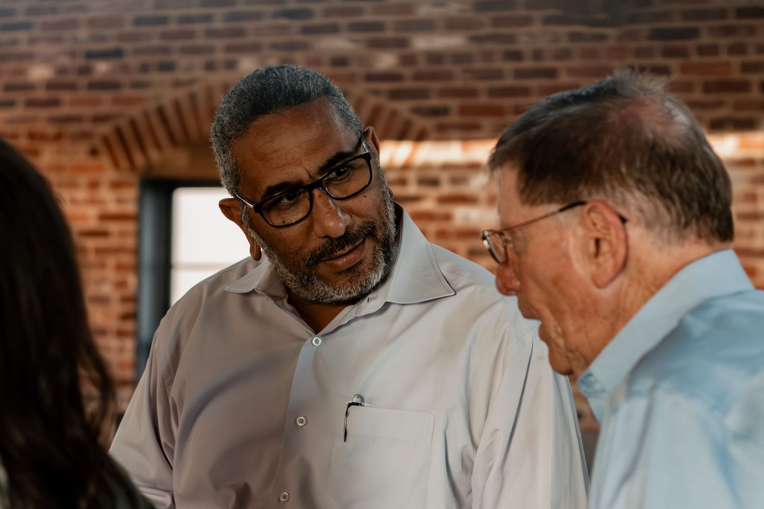 Two people talking and laughing together at a casual gathering with red brick wall visible in background.