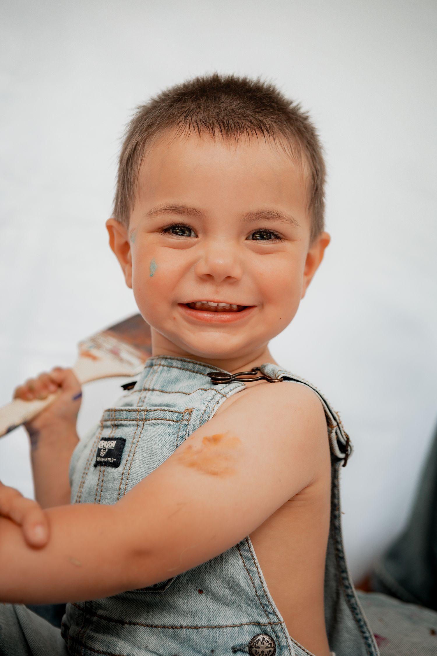 Happy child wearing blue denim overalls smiles brightly in natural light.