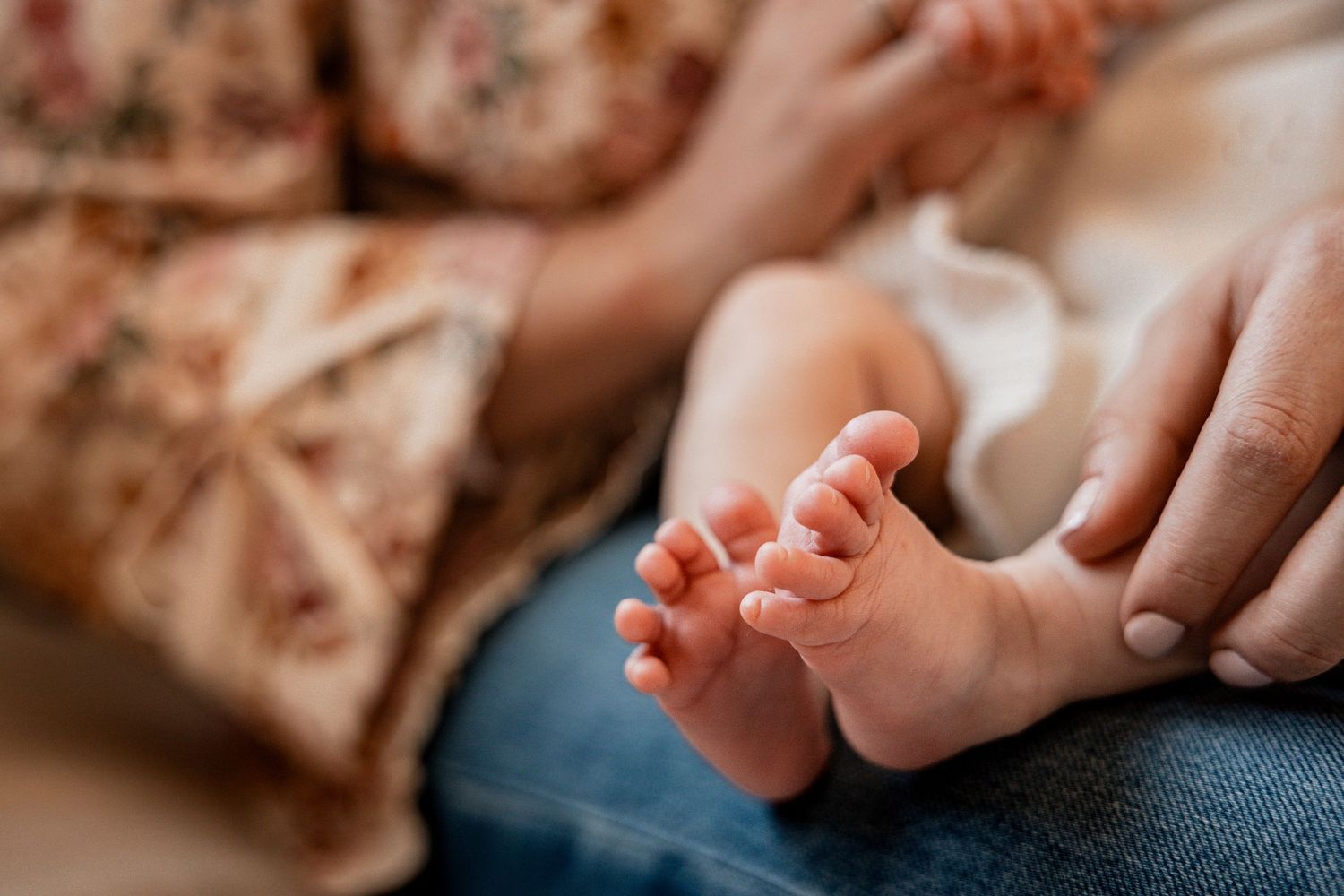 Close-up of tiny newborn baby feet held gently by a parent's hands, with soft floral background.