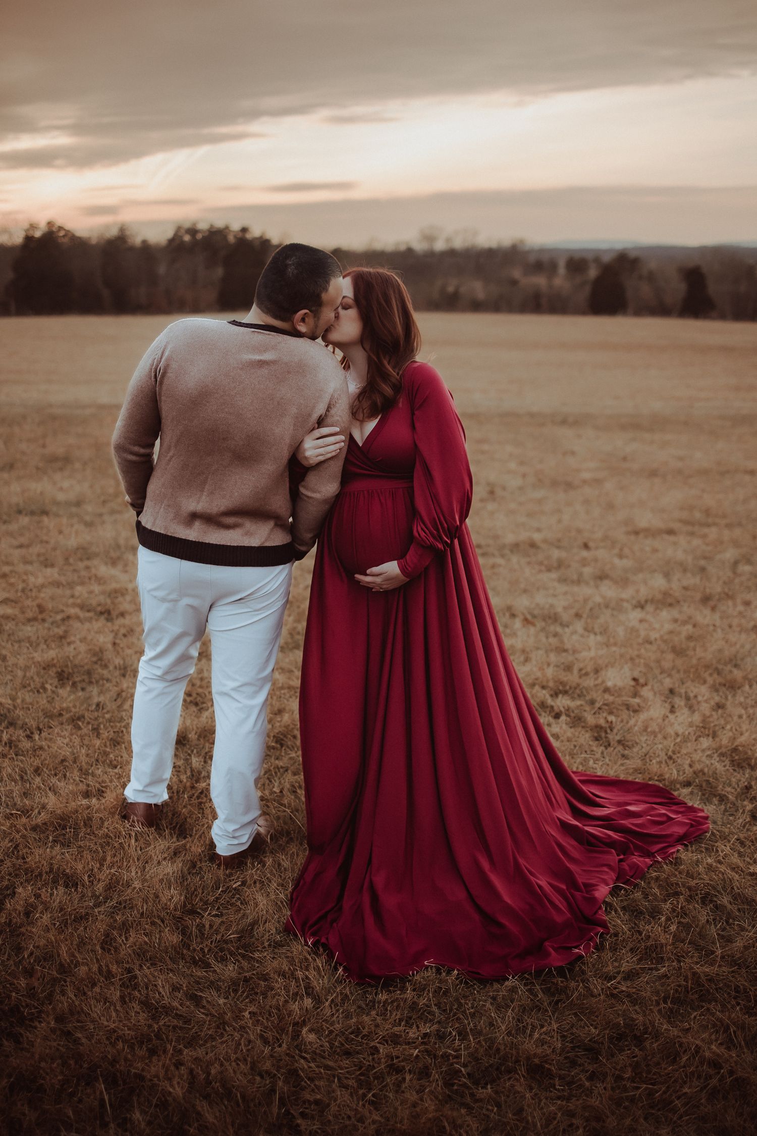 A couple in a field at sunset, with one wearing a flowing burgundy dress creating a romantic silhouette.
