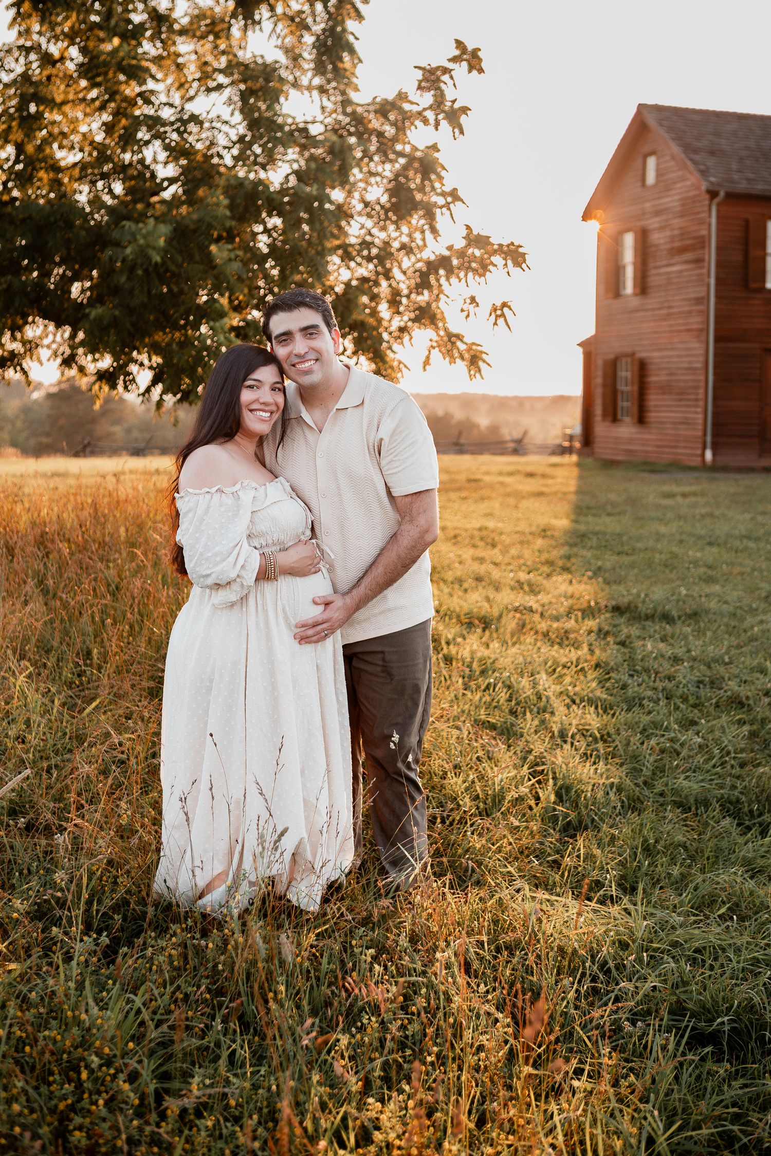 A romantic sunset portrait in a golden field with a rustic wooden farmhouse in the background.