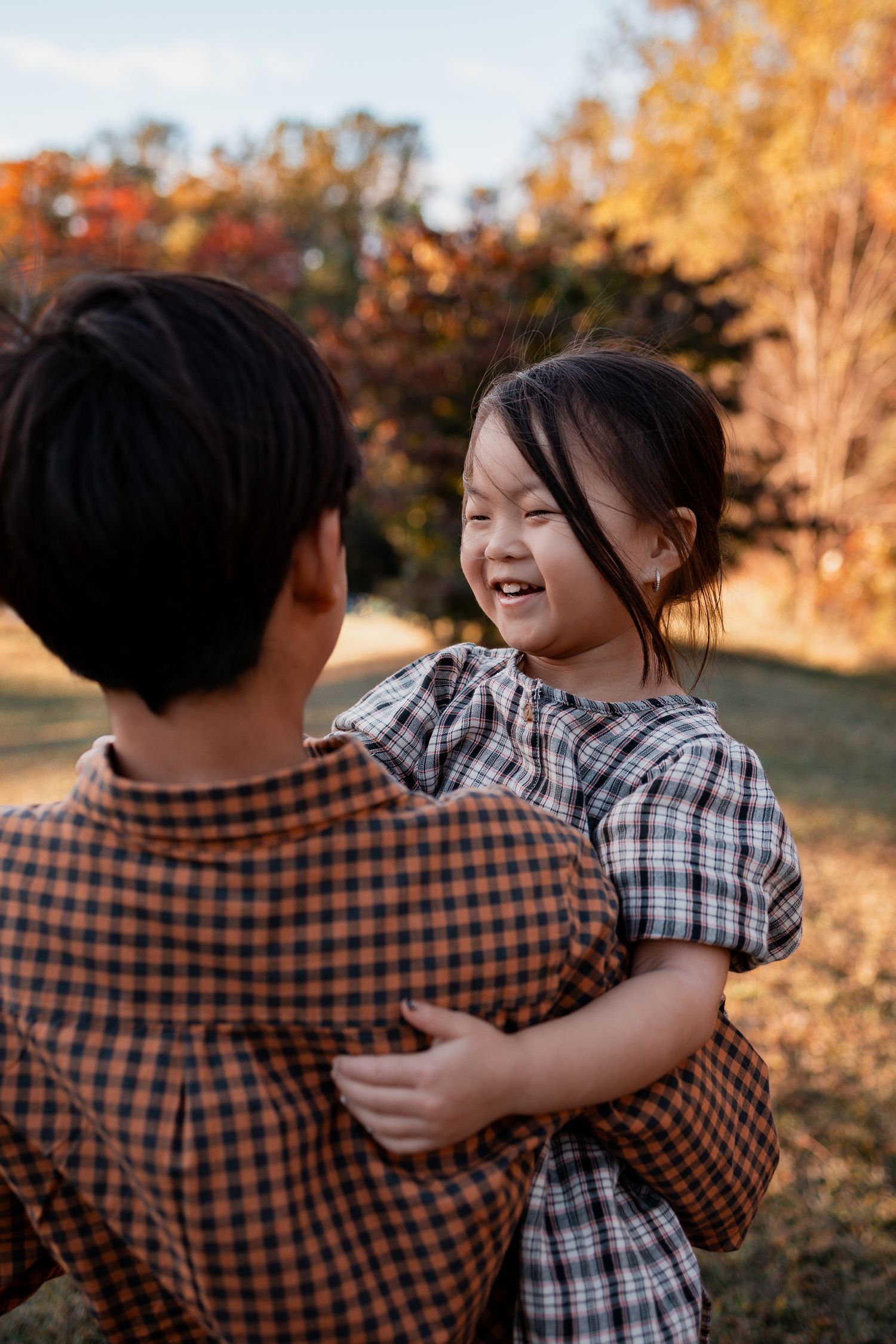 Two people wearing plaid shirts share warm embraces in a golden-lit outdoor setting during sunset.