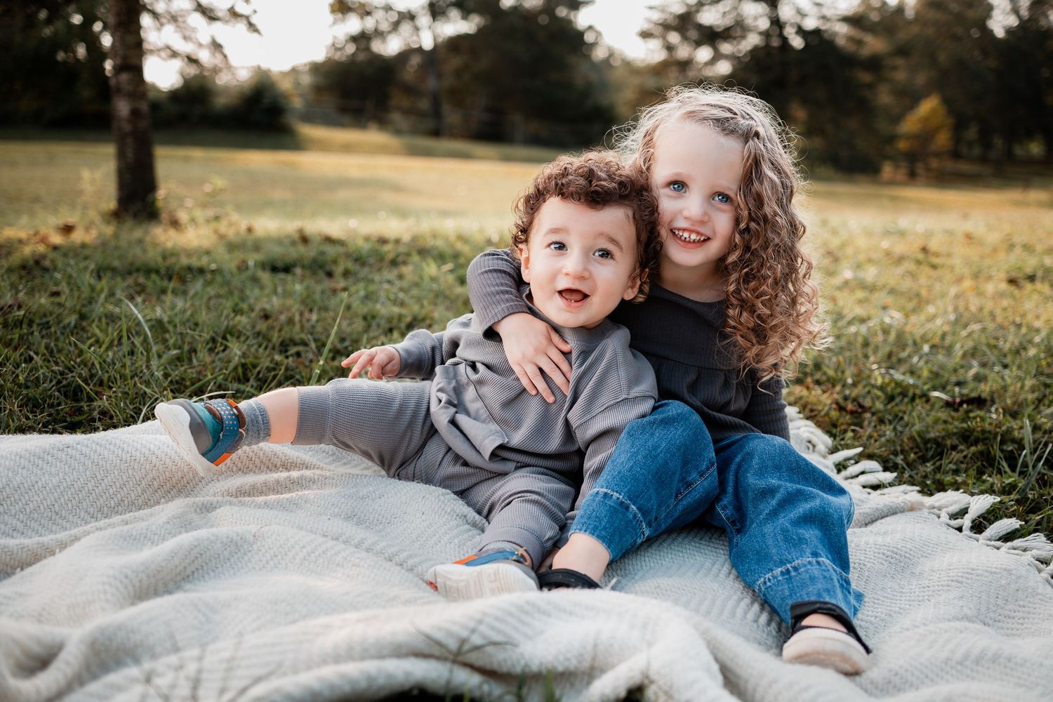 A family lying on a blanket outdoors enjoying a warm autumn day in a grassy field at sunset.