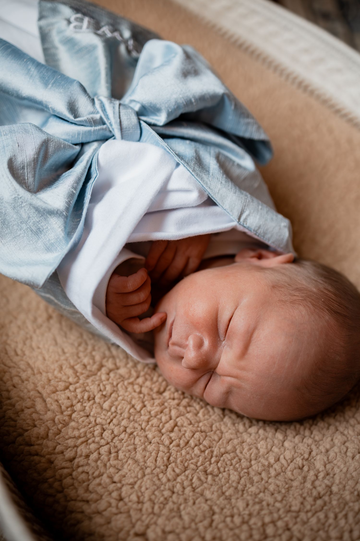 Close-up of sleeping newborn baby wrapped in blue bow blanket on beige surface.