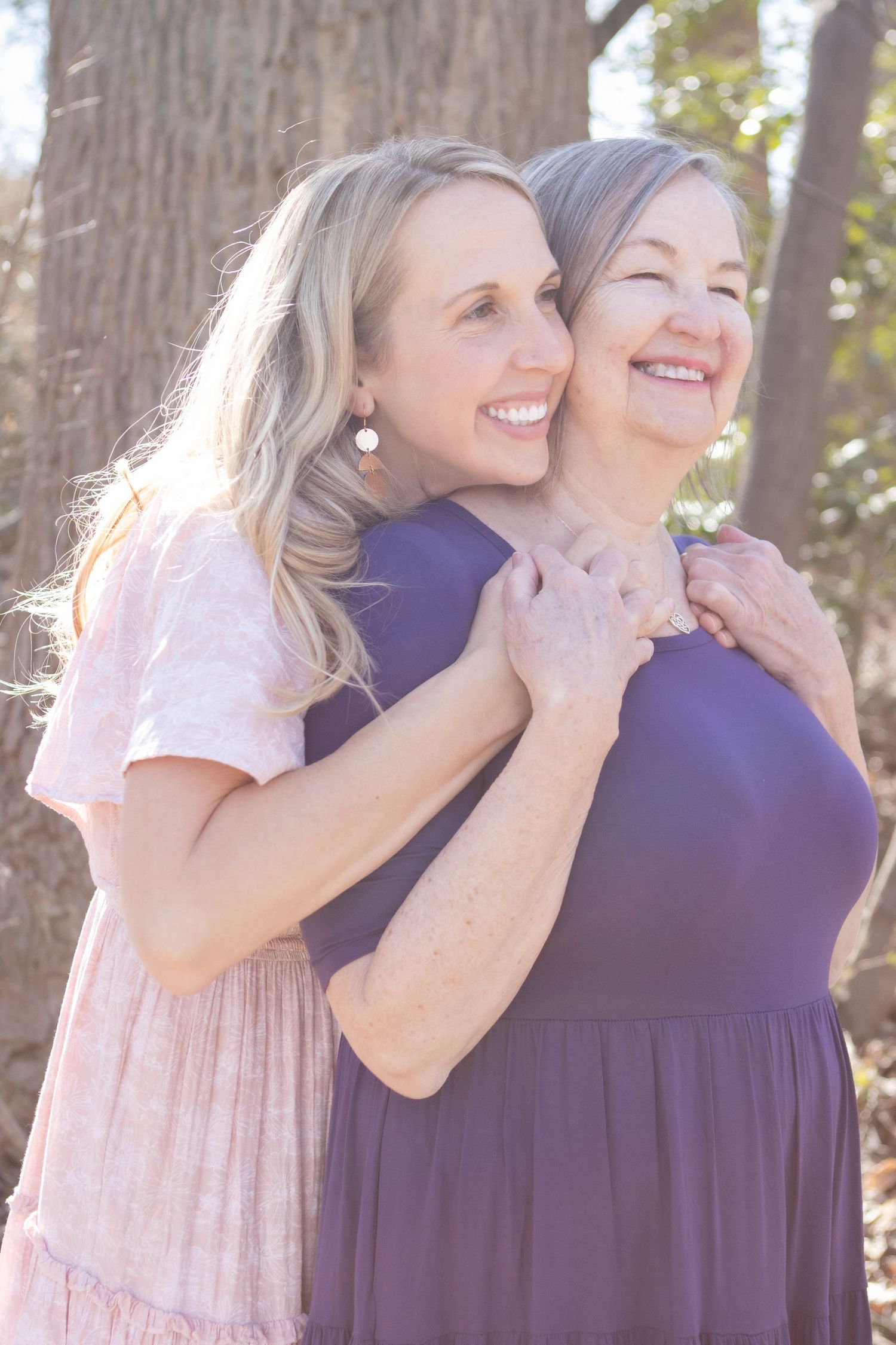 Two people sharing a joyful hug and laughter outdoors against a tree backdrop.