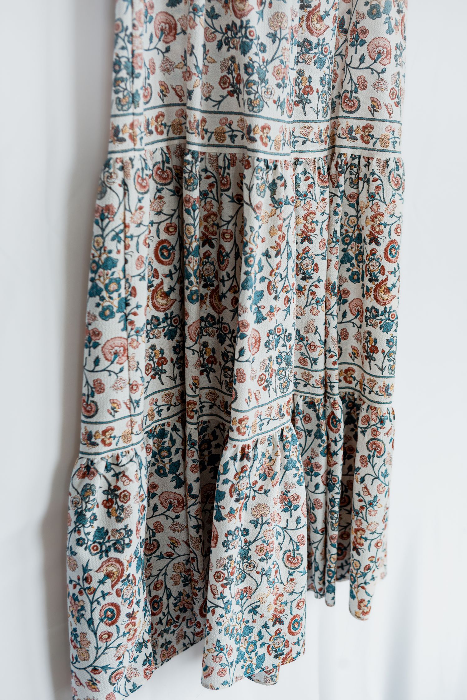 Floral printed maxi skirt with blue and brown paisley pattern on cream background hangs against white wall.