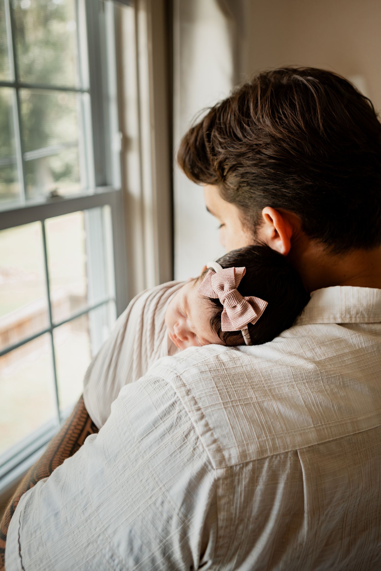 Tender moment by a window as two people embrace in soft natural light, with a gentle kiss on the head.