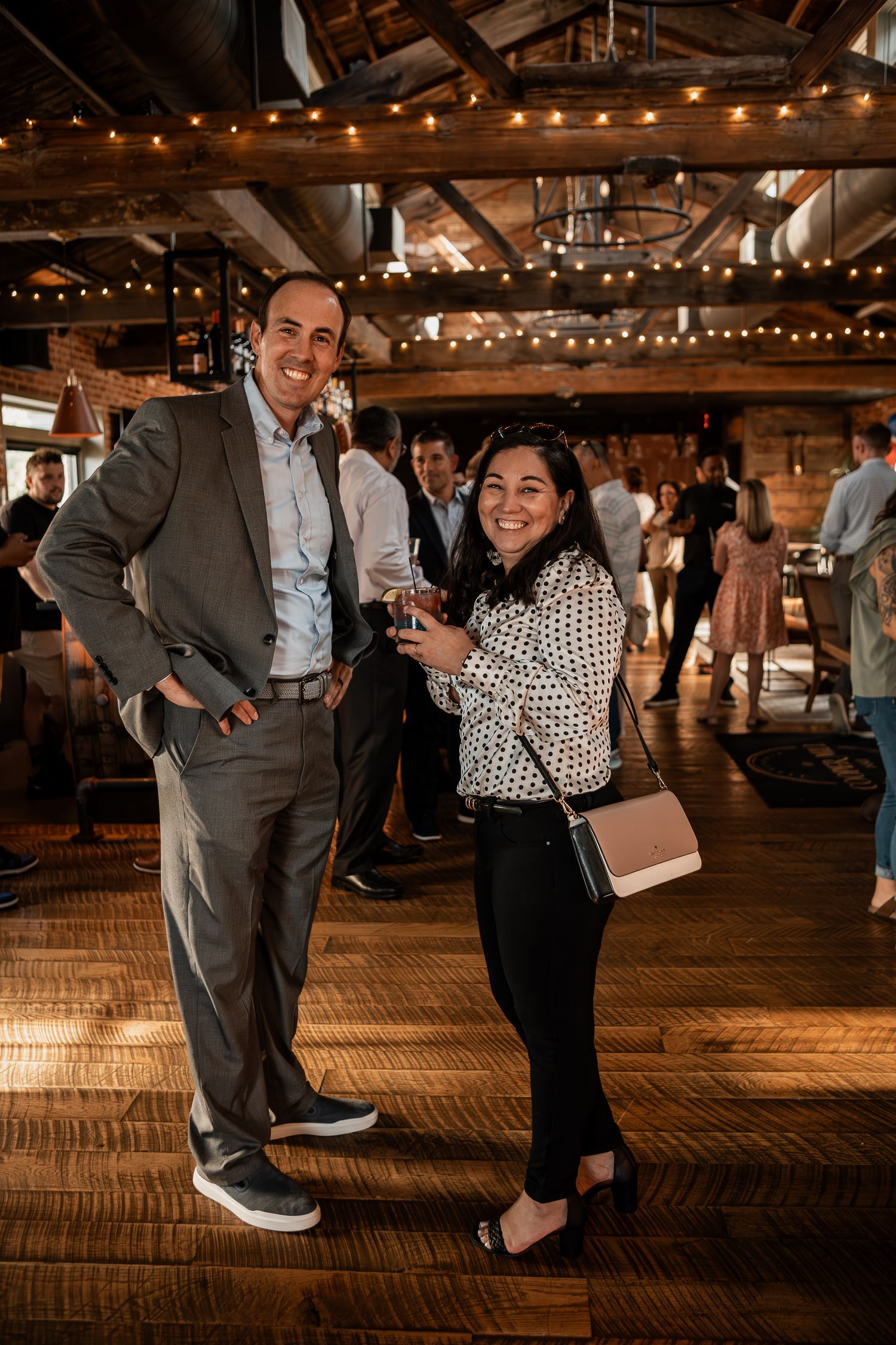 Two guests enjoying a celebration in an industrial-style venue with string lights and exposed brick walls.