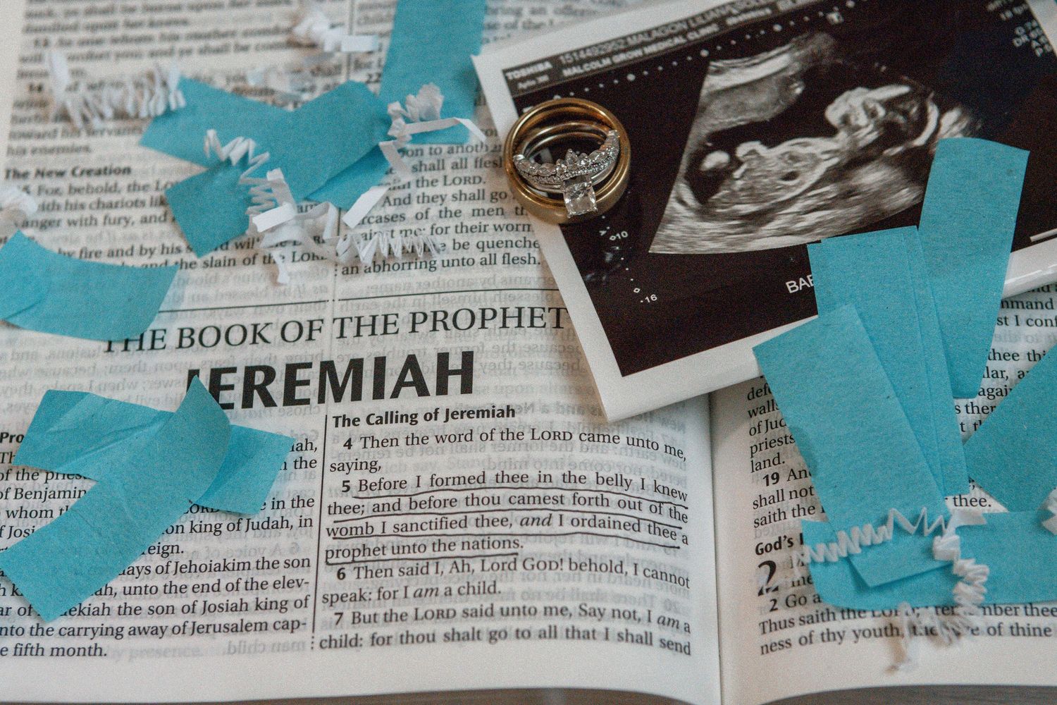 An open Bible showing the Book of Jeremiah with blue paper cutouts decorating the pages alongside ultrasound photos.